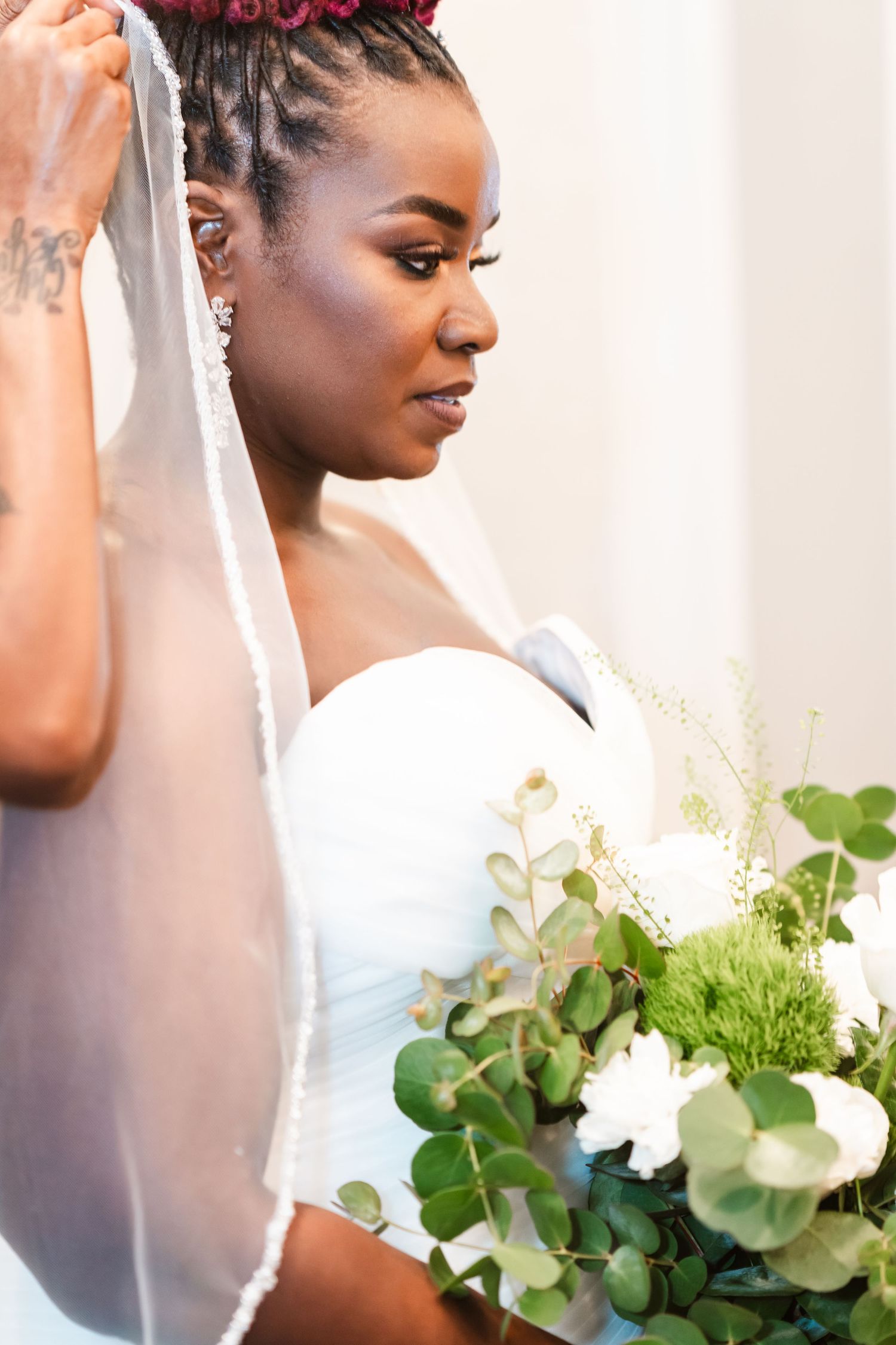 A bridal portrait showing an elegant white wedding gown and bouquet with greenery.