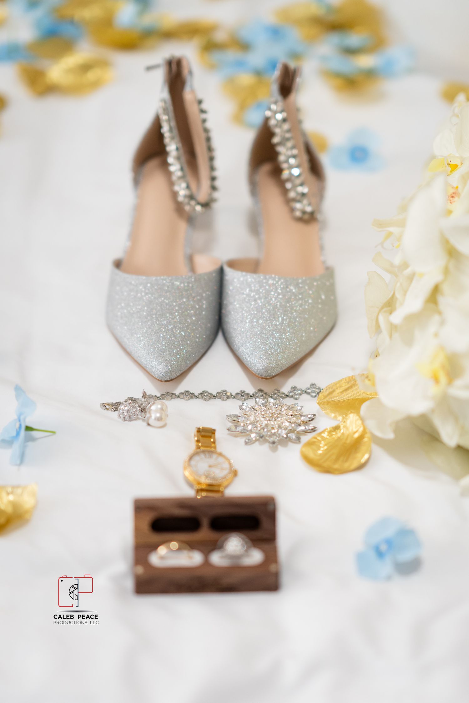 Elegant silver sparkly wedding shoes and jewelry arranged with delicate floral accents and wooden display box.