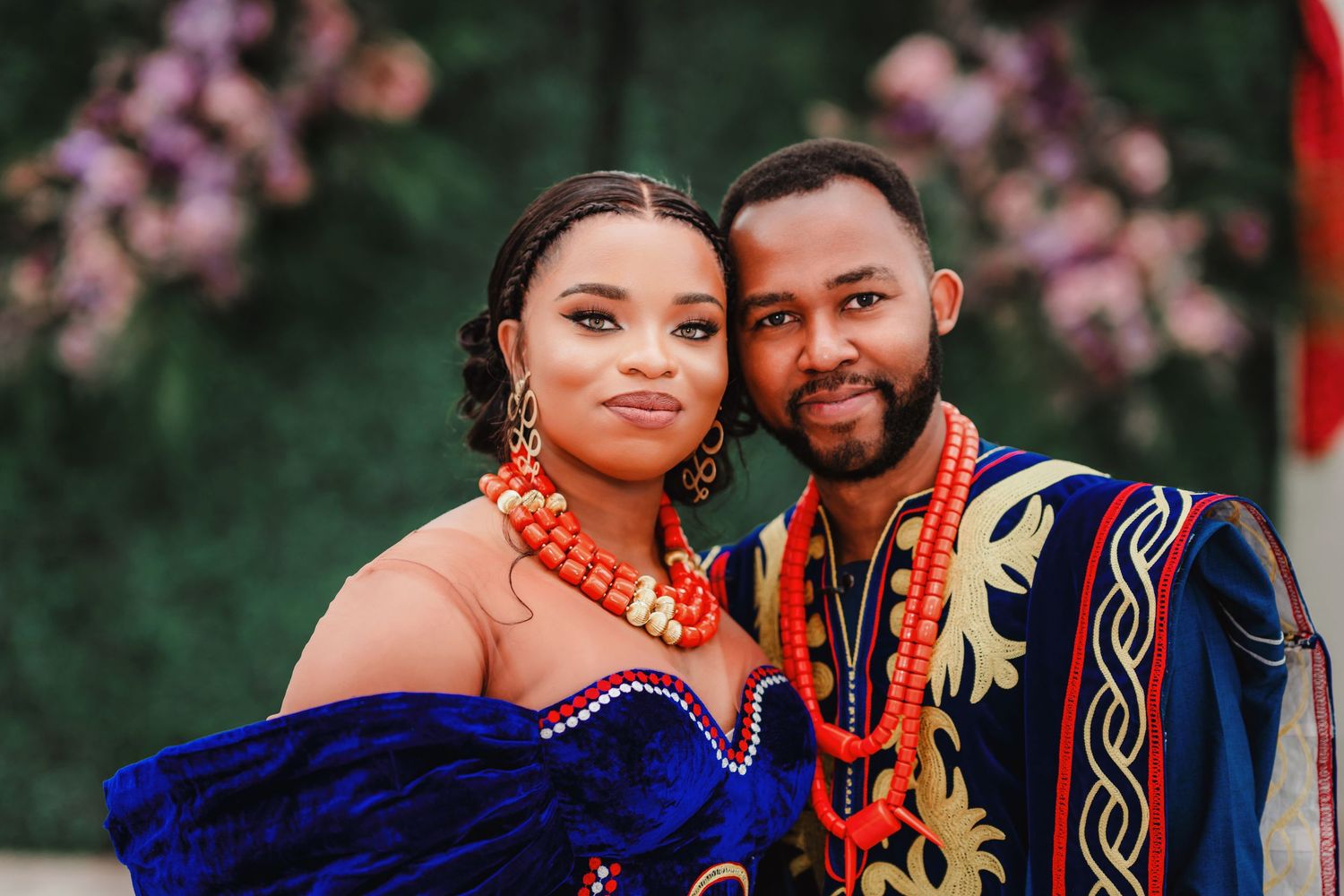 A close-up portrait of a couple in matching blue and orange African-inspired formal attire.