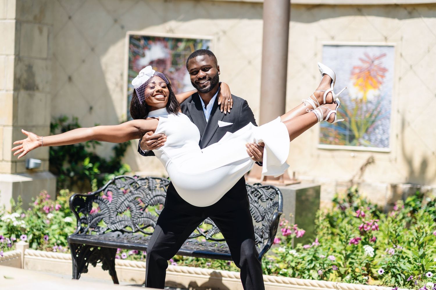 A couple strikes a dramatic dance pose together in a garden setting with stone columns and flowers.