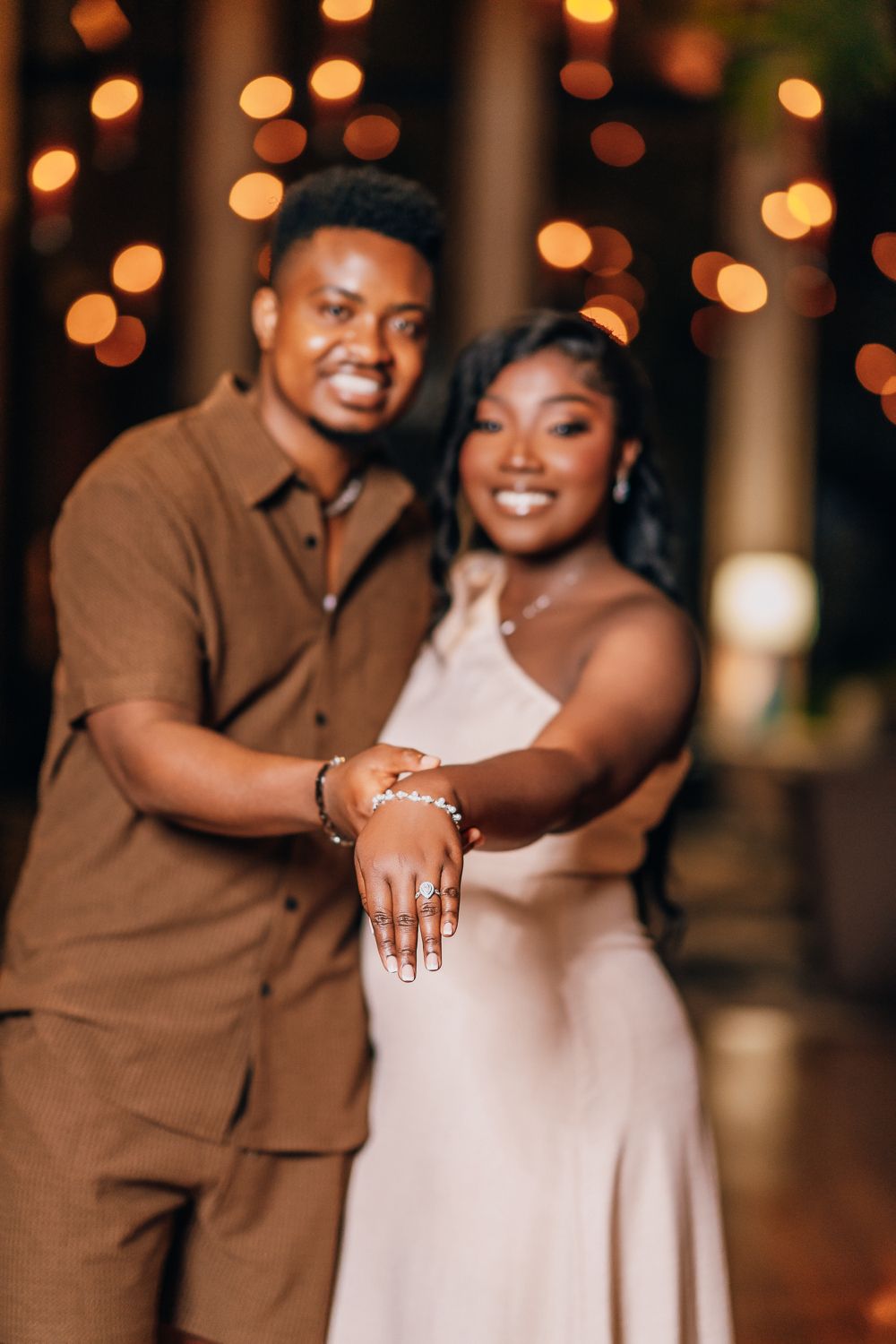 A joyful couple laughs together during their engagement shoot under ambient string lights.