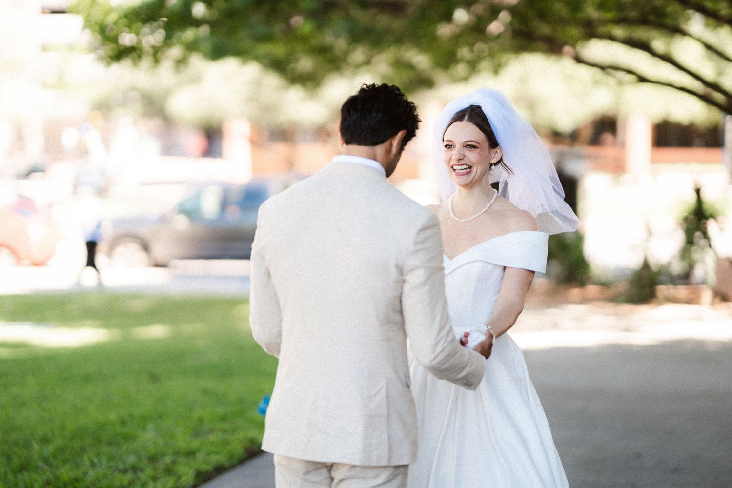 A wedding party poses outdoors in a garden setting with greenery and natural light.