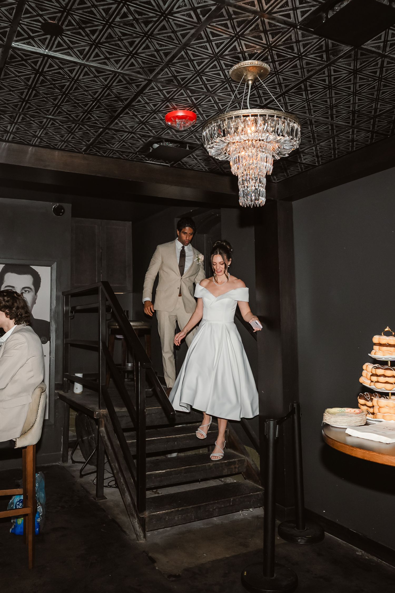 Wedding reception scene in dark room with ornate ceiling and chandelier lighting.