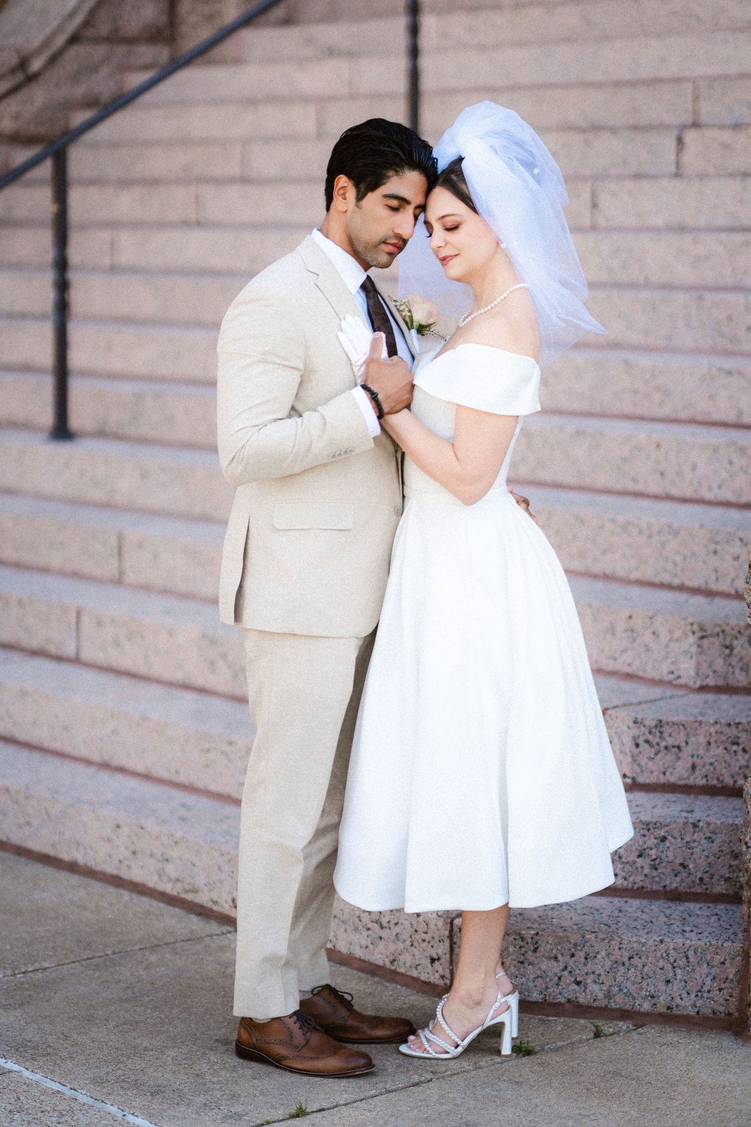 A romantic wedding couple poses on stone steps with the bride in a short white dress.