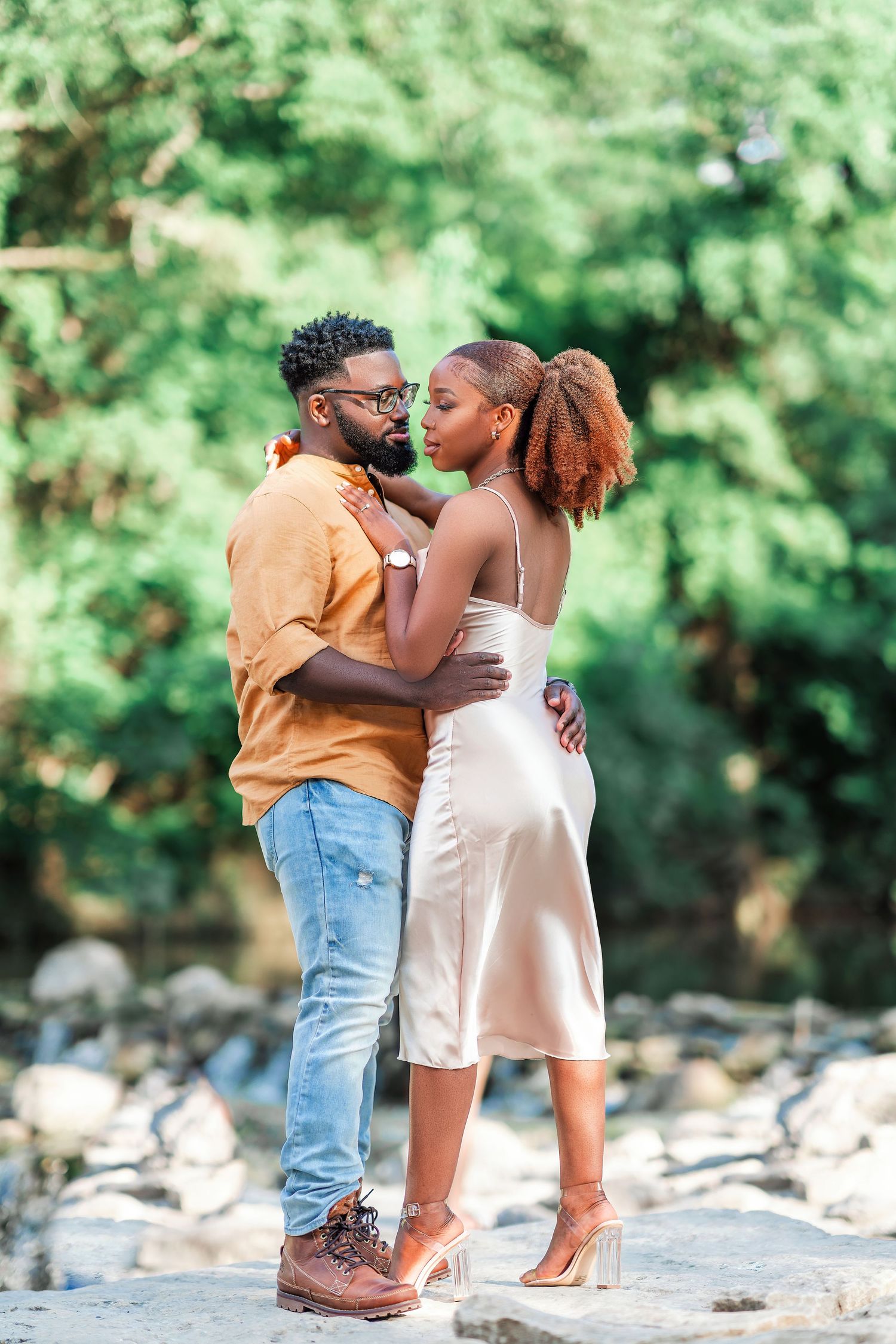 A couple stands together on rocky terrain surrounded by greenery.