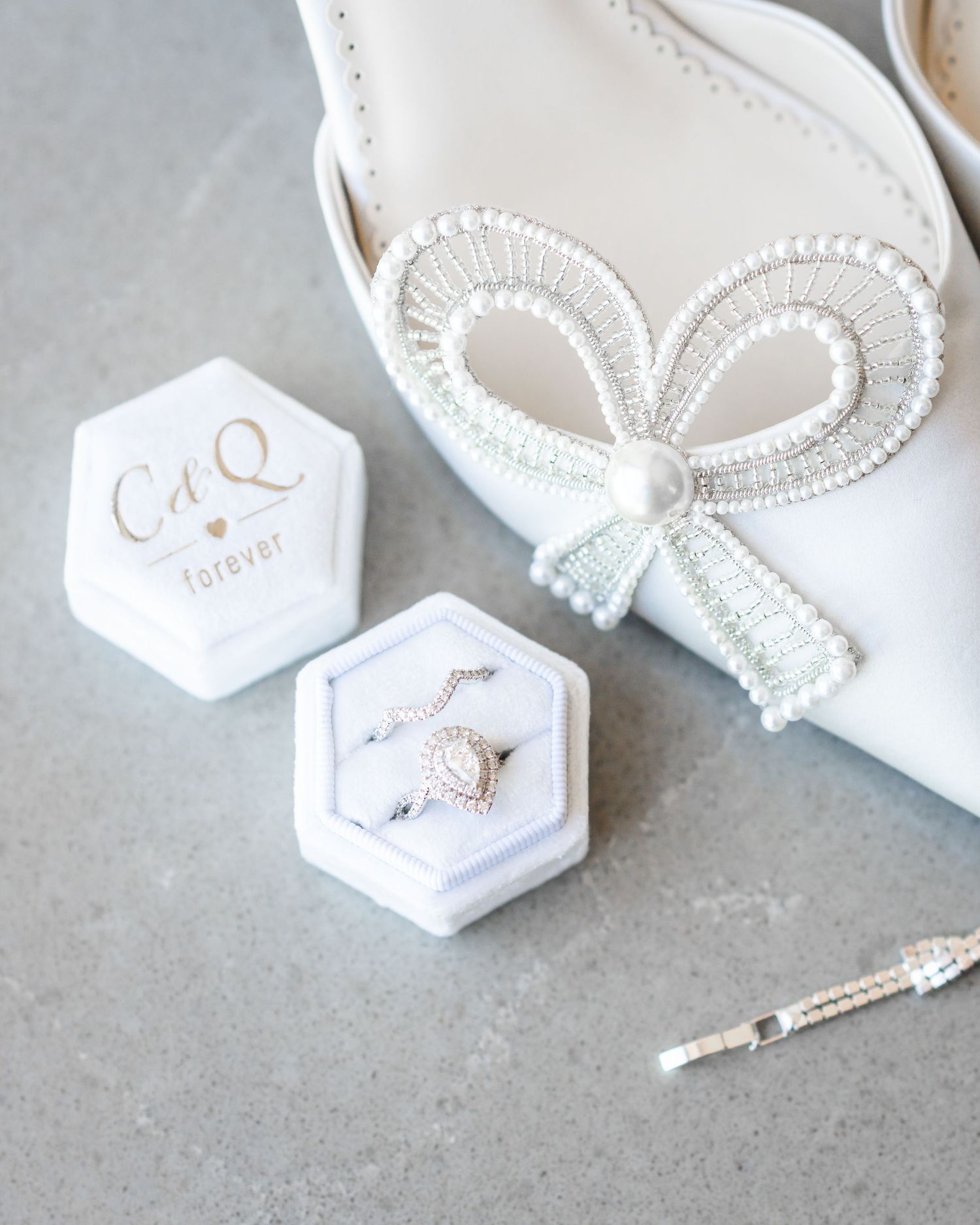 White bridal accessories including pearl-adorned shoes and hexagonal jewelry boxes on gray surface.