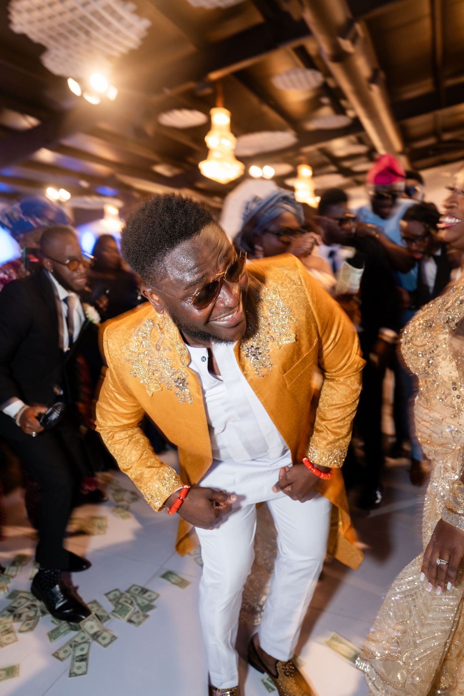 Wedding party dancing on money-covered dance floor with guests in formal attire.