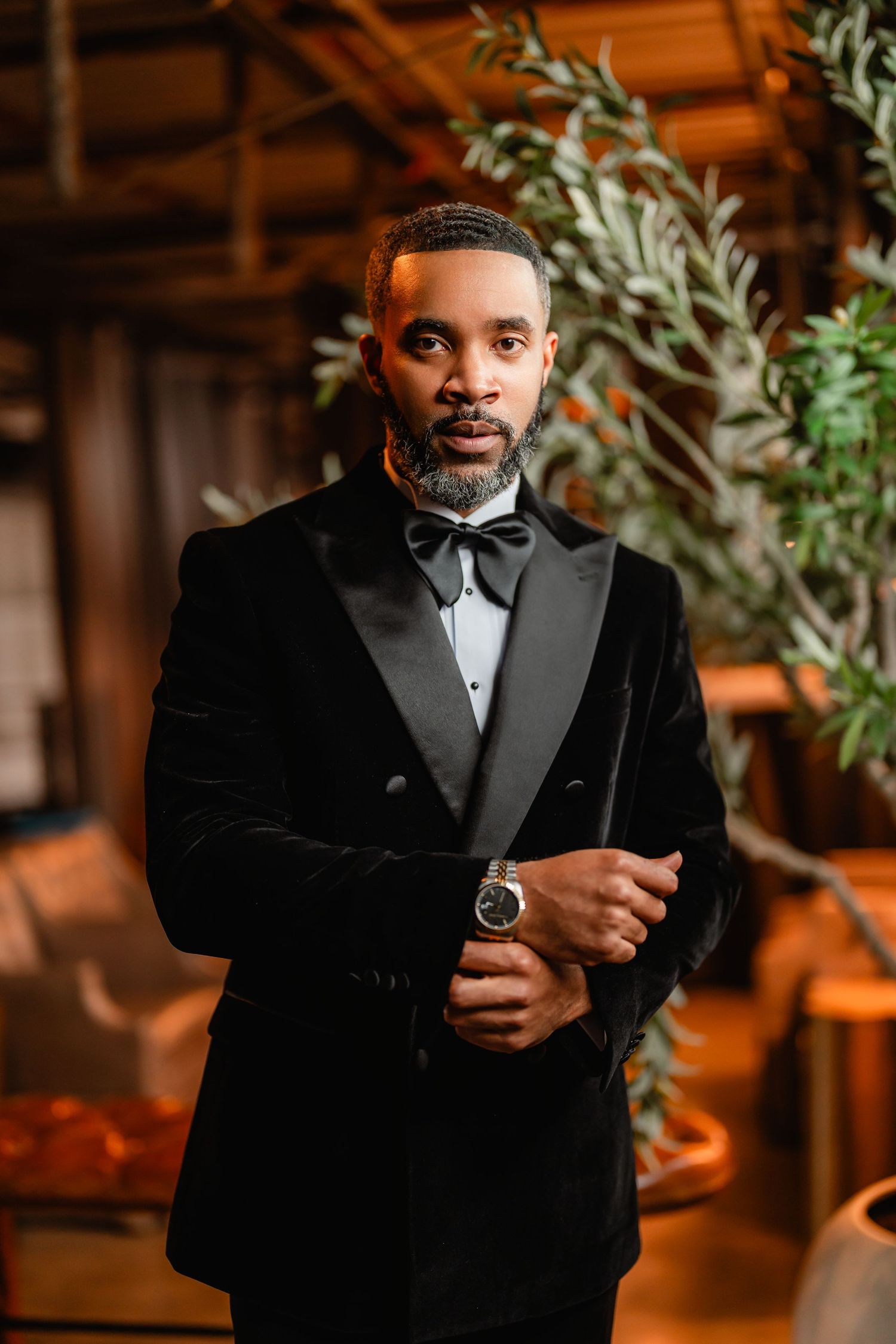 A person in a black tuxedo and bow tie smiles during an indoor wedding reception.