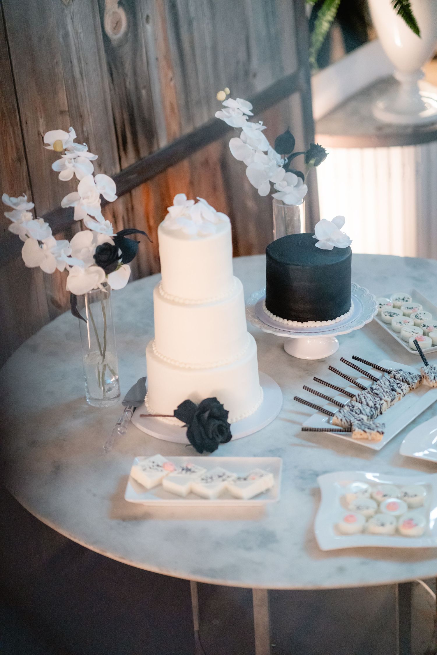Elegant white and black wedding cakes with floral decorations displayed on a dessert table.