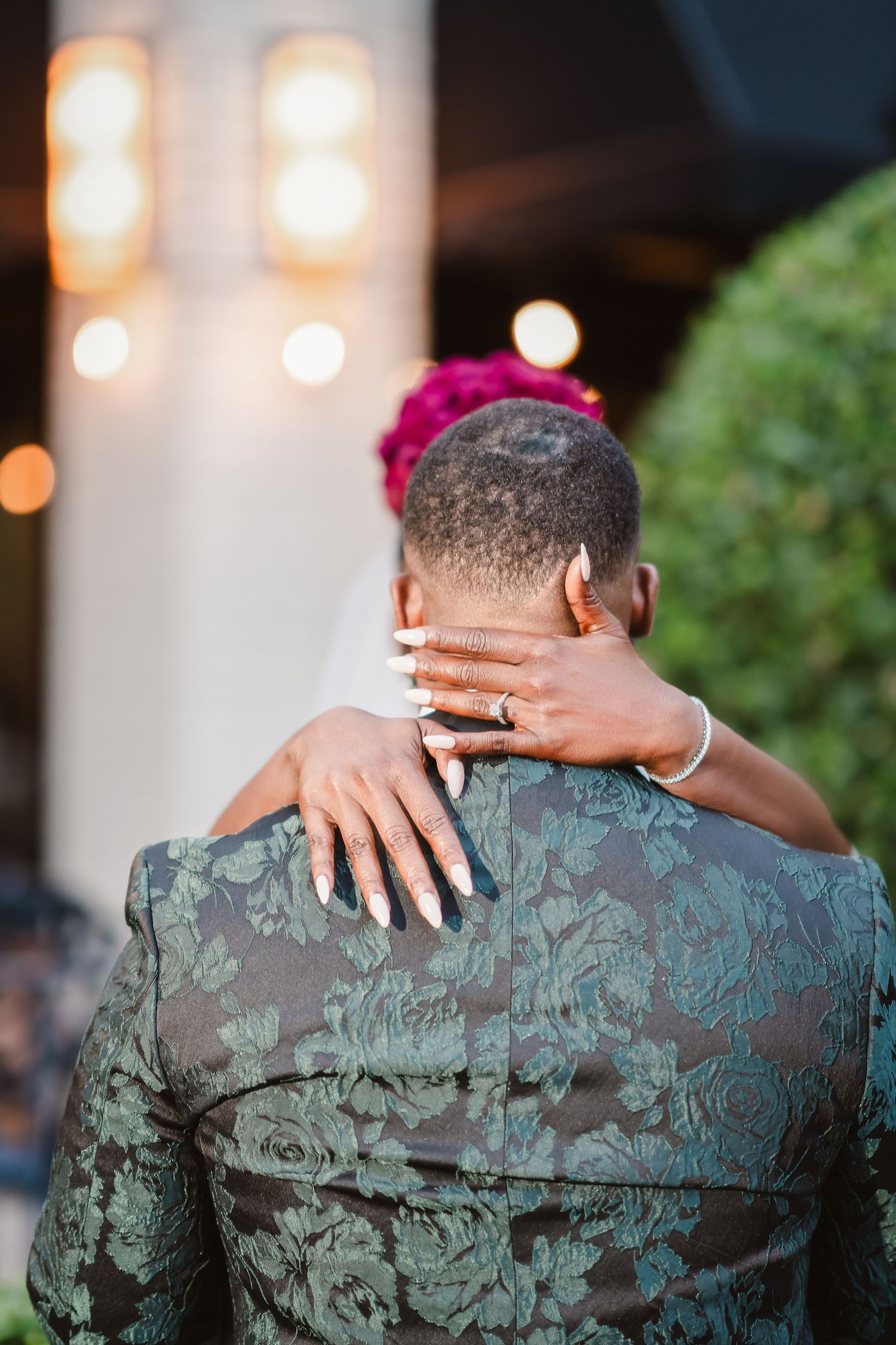 Close-up detail of hands embracing on a textured emerald green wedding jacket.
