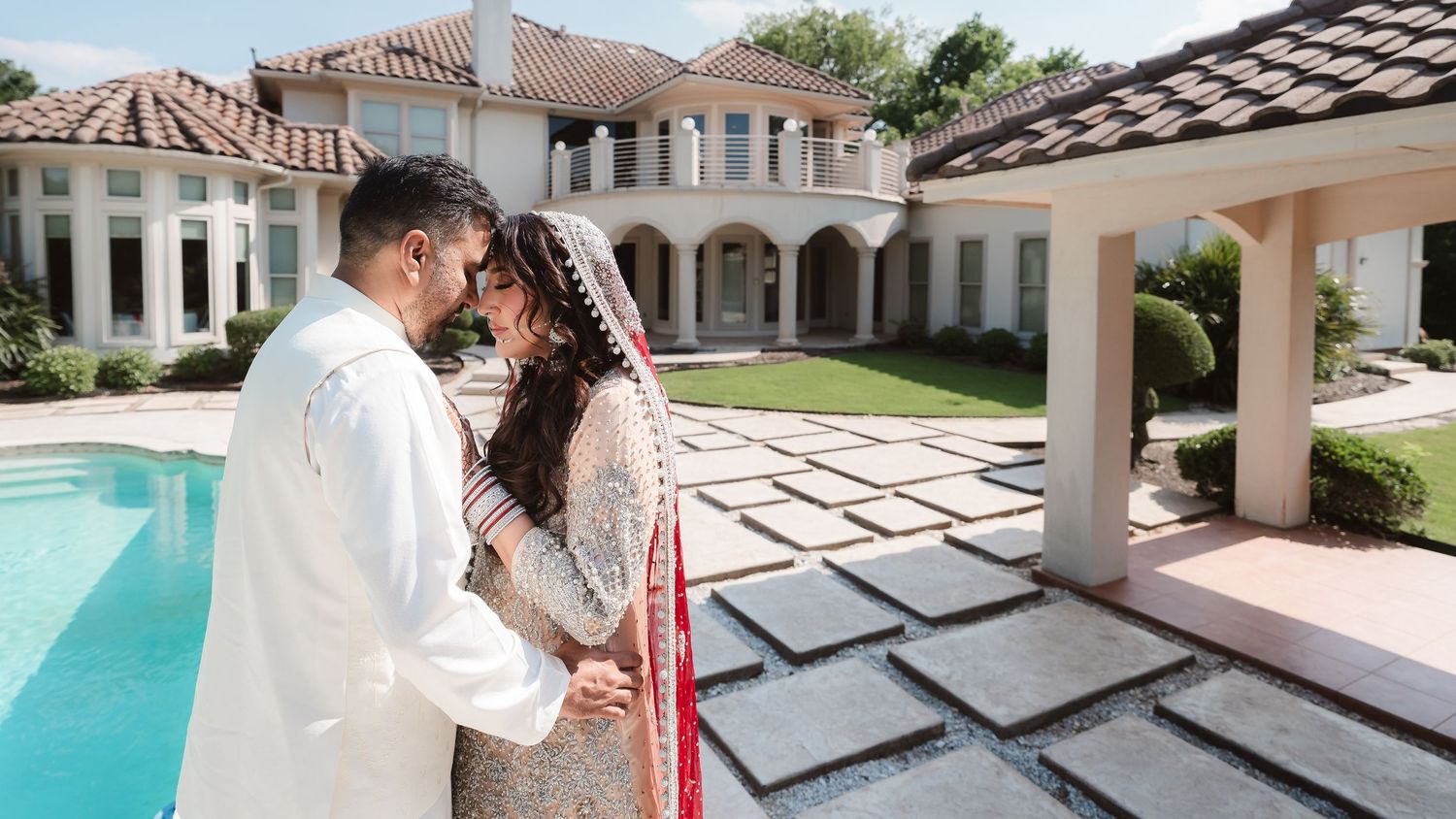 Panoramic view of a luxurious Mediterranean-style villa with white columns and a sparkling turquoise swimming pool.