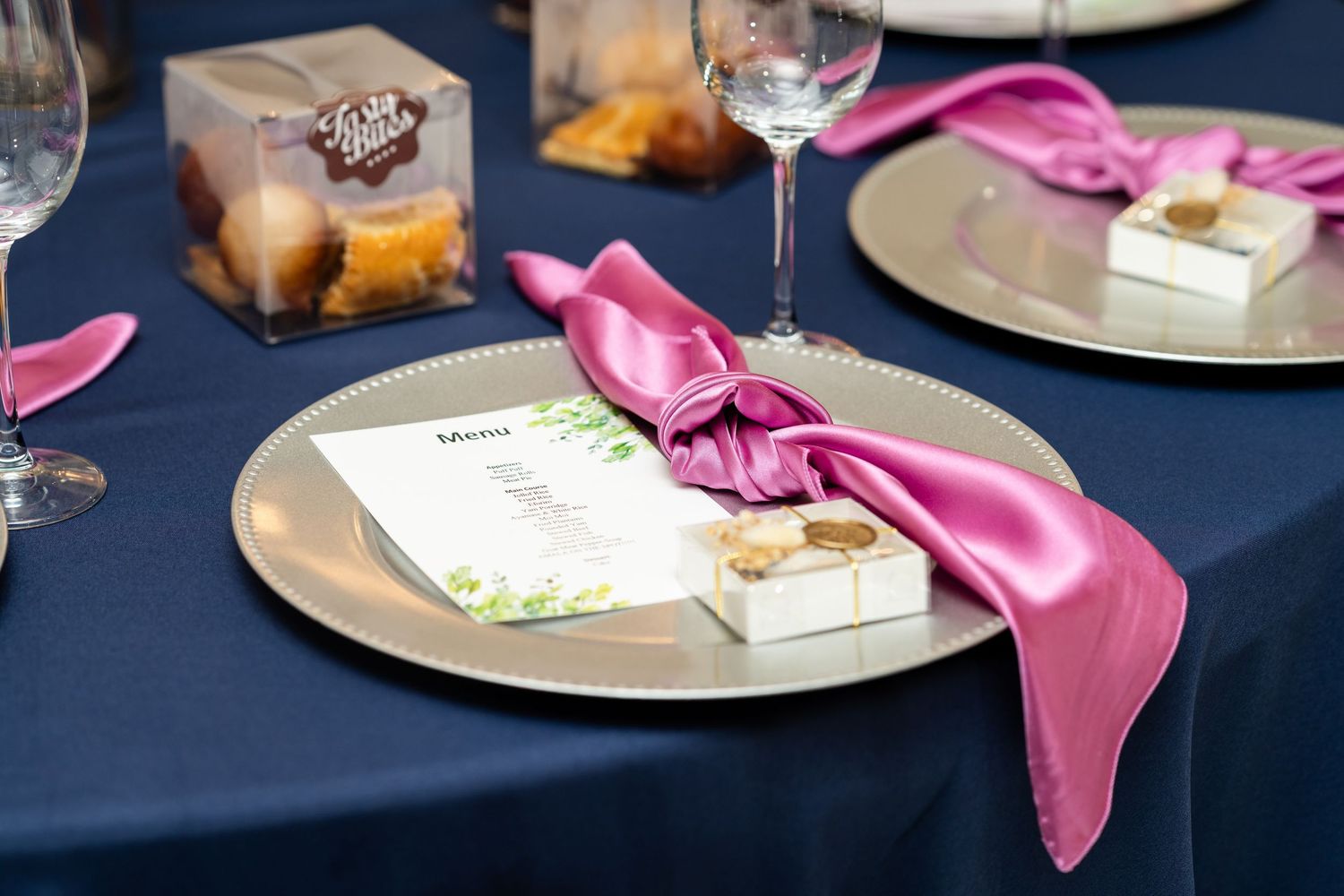 Pink satin napkins and wine glasses adorn an elegant table setting with a dark blue tablecloth.