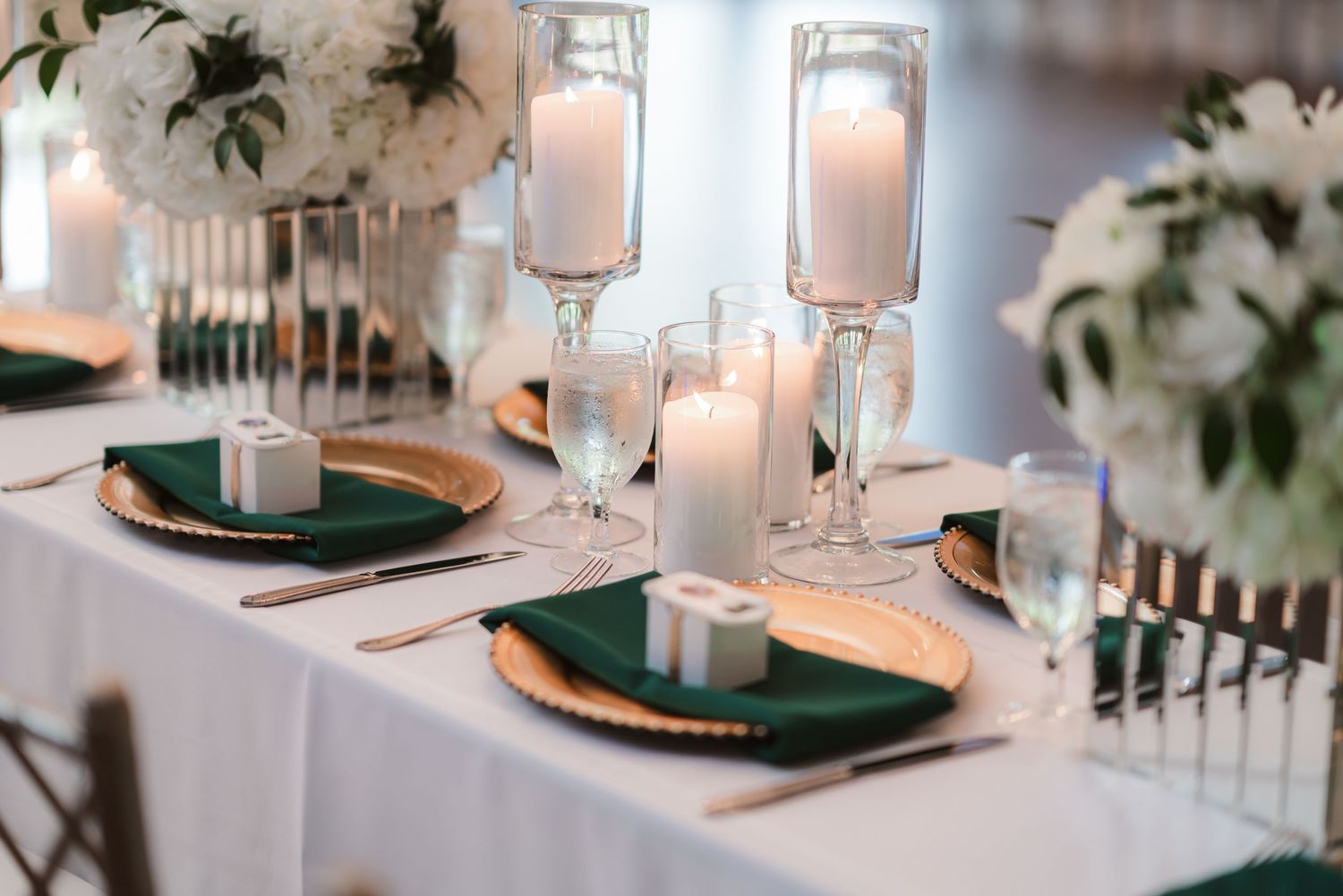 Elegant wedding reception table setting with white linens, greenery and glowing candle centerpieces.