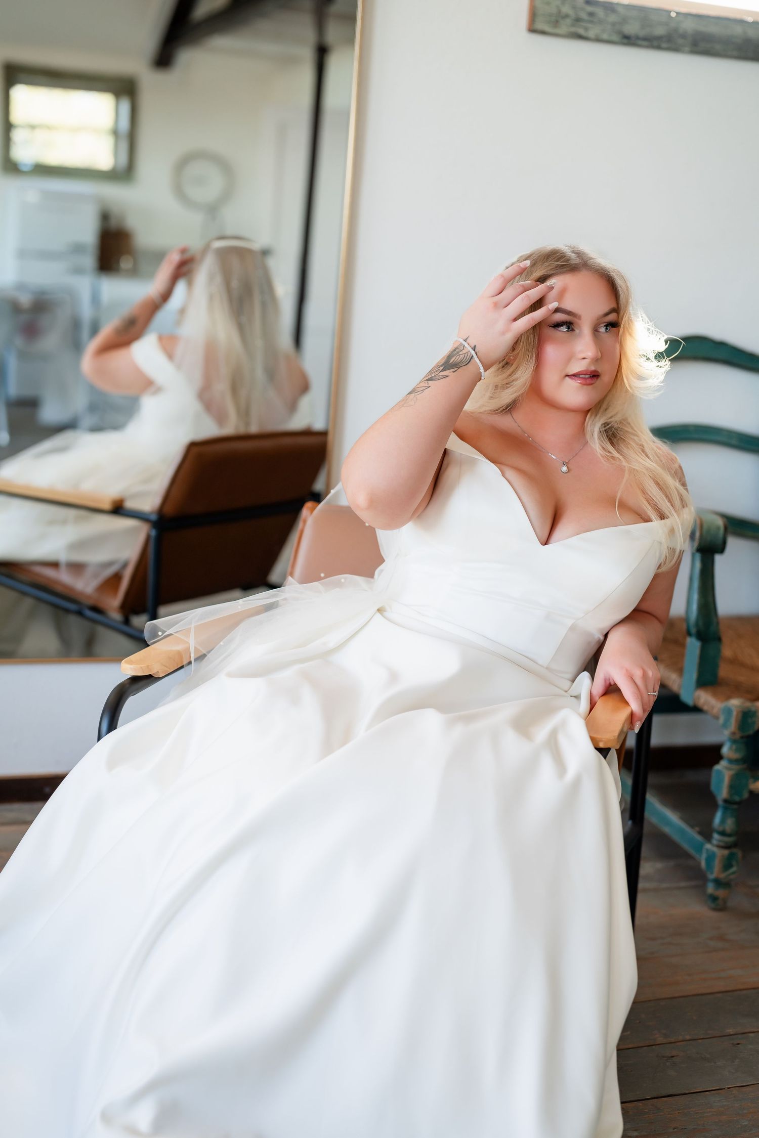 A bride in a flowing white dress poses gracefully on vintage wooden floors in natural light.