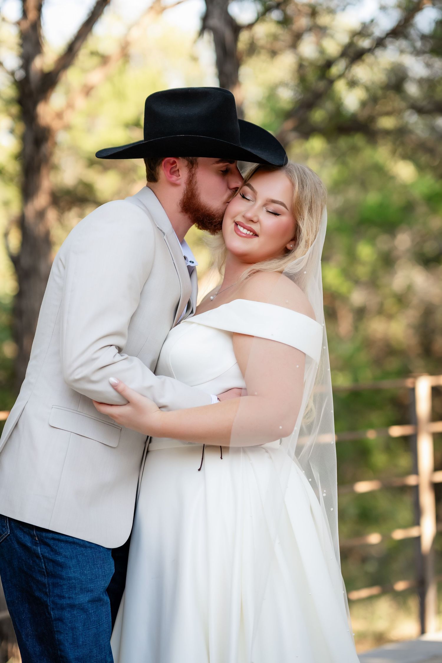 Romantic outdoor wedding portrait with couple embracing in rustic attire.