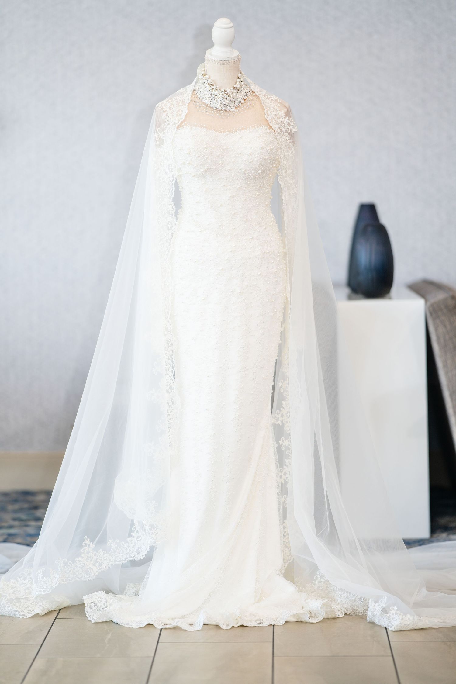 Ethereal white wedding dress with flowing cape and delicate lace details on display.