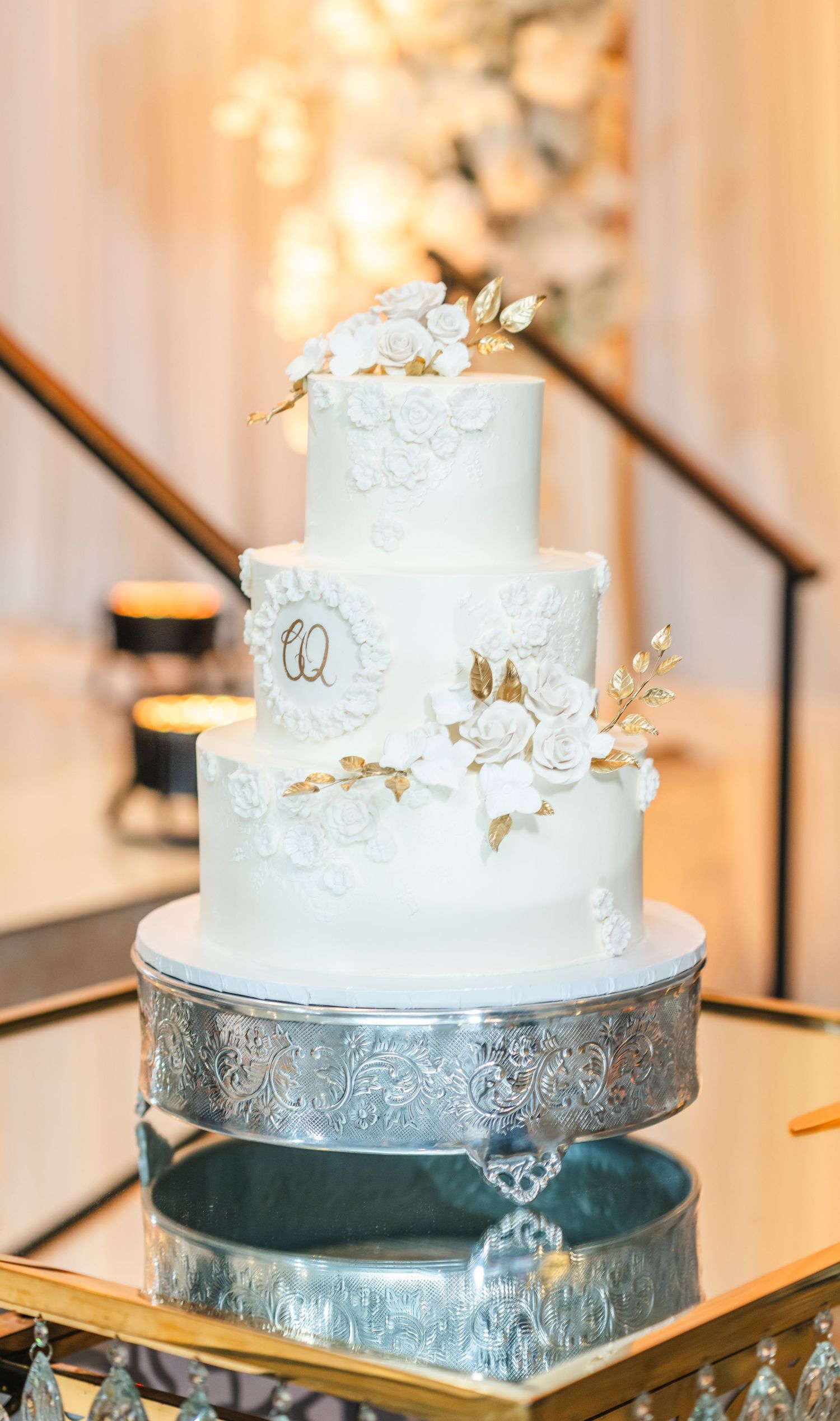 Elegant white wedding cake with delicate floral details displayed on silver and gold stand.