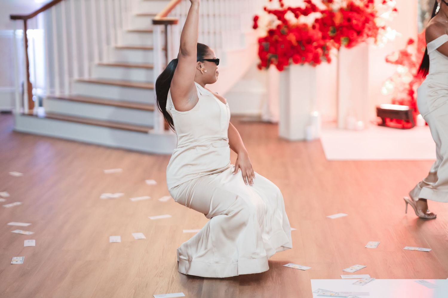 A bride in a white gown dances on a hardwood floor with rose petals scattered around.