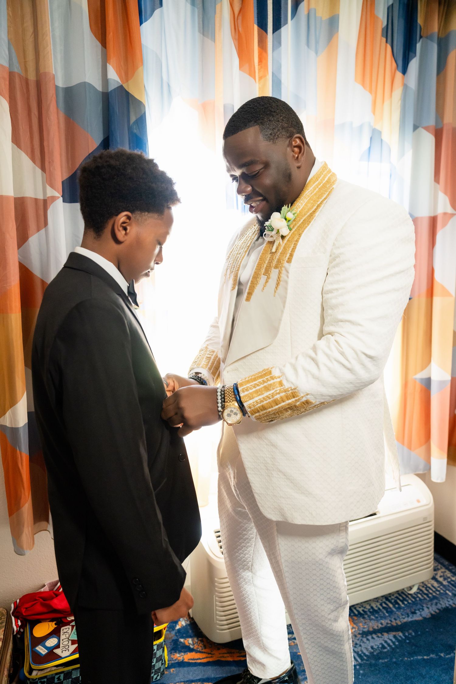 Getting ready scene with formal attire adjustments in orange and blue decorated room.