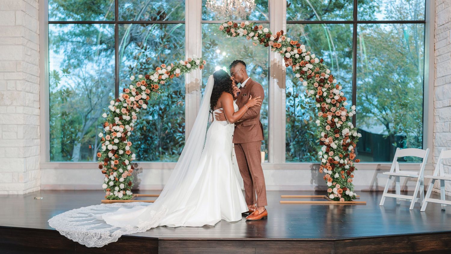 Wedding ceremony setup with floral arch and natural light streaming through large windows.