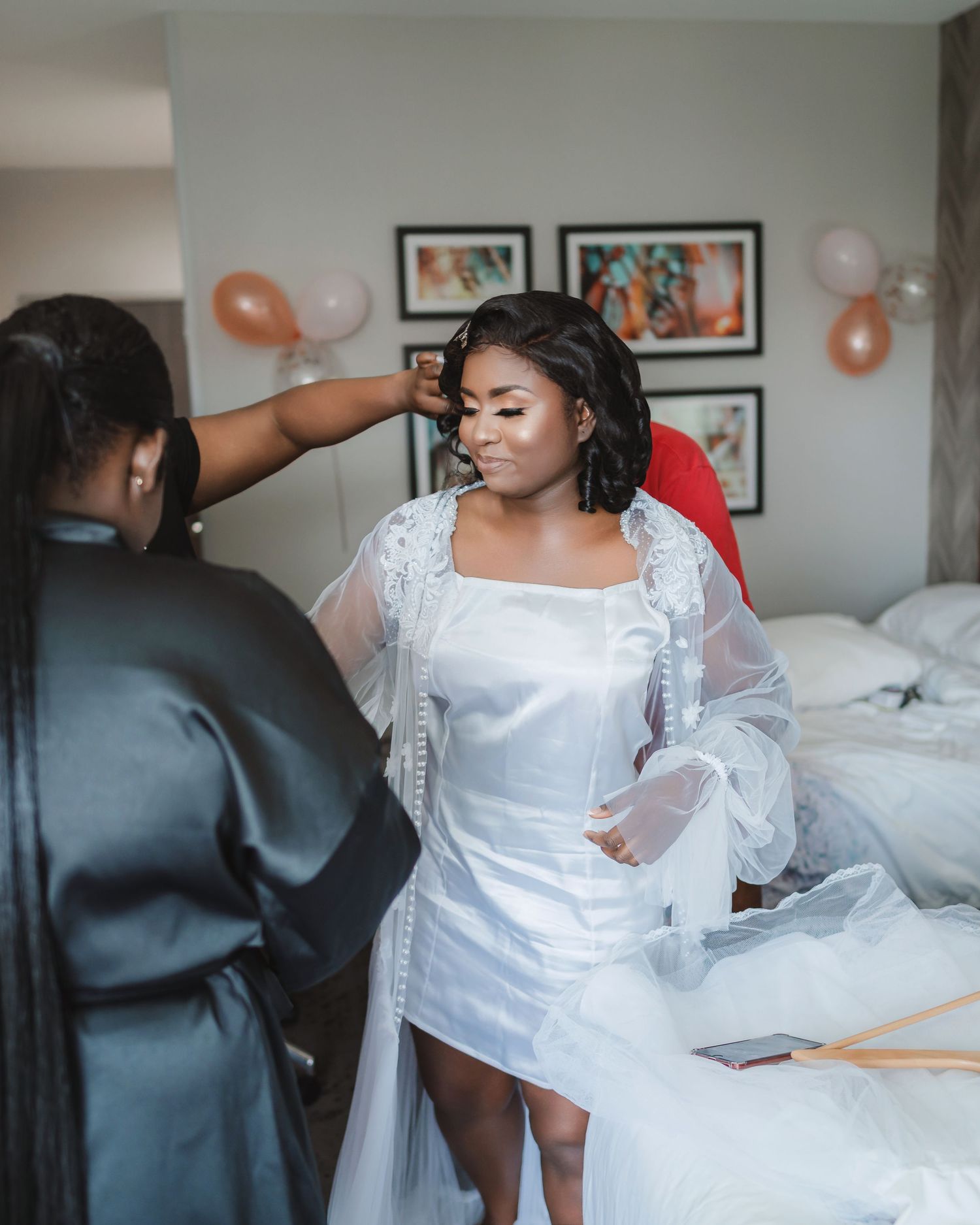 Wedding preparation scene showing white formal attire in a room with orange balloons and framed artwork.