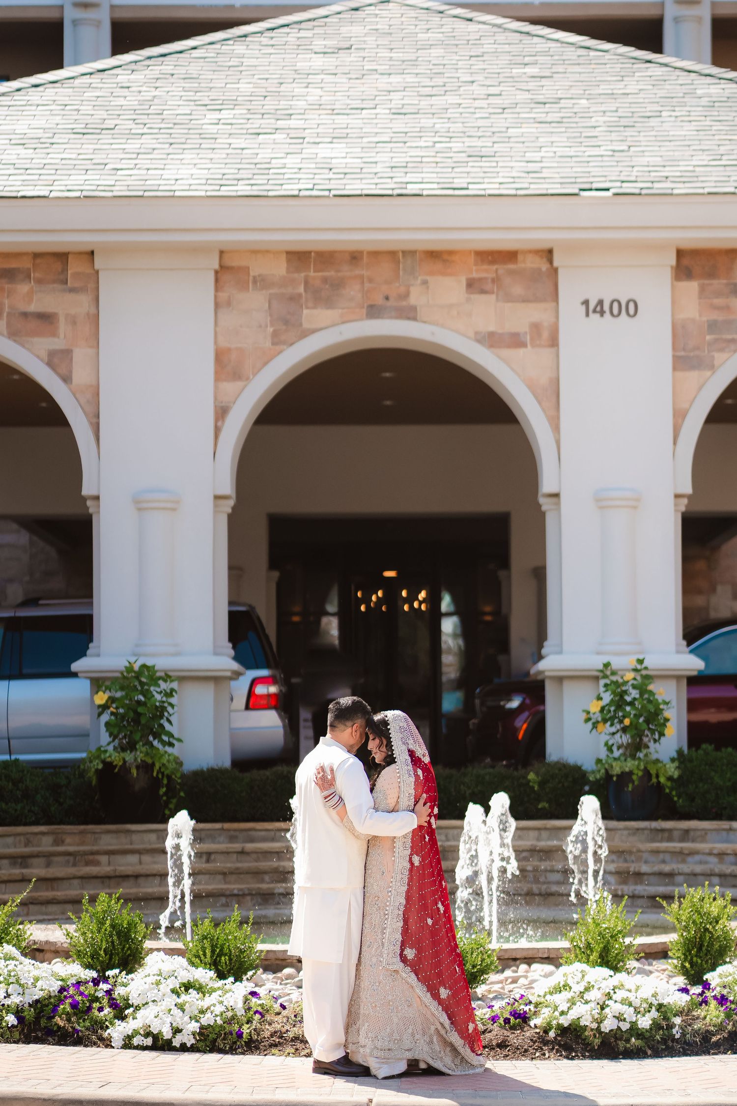Wedding couple walking under white archways with landscaped gardens in the foreground.