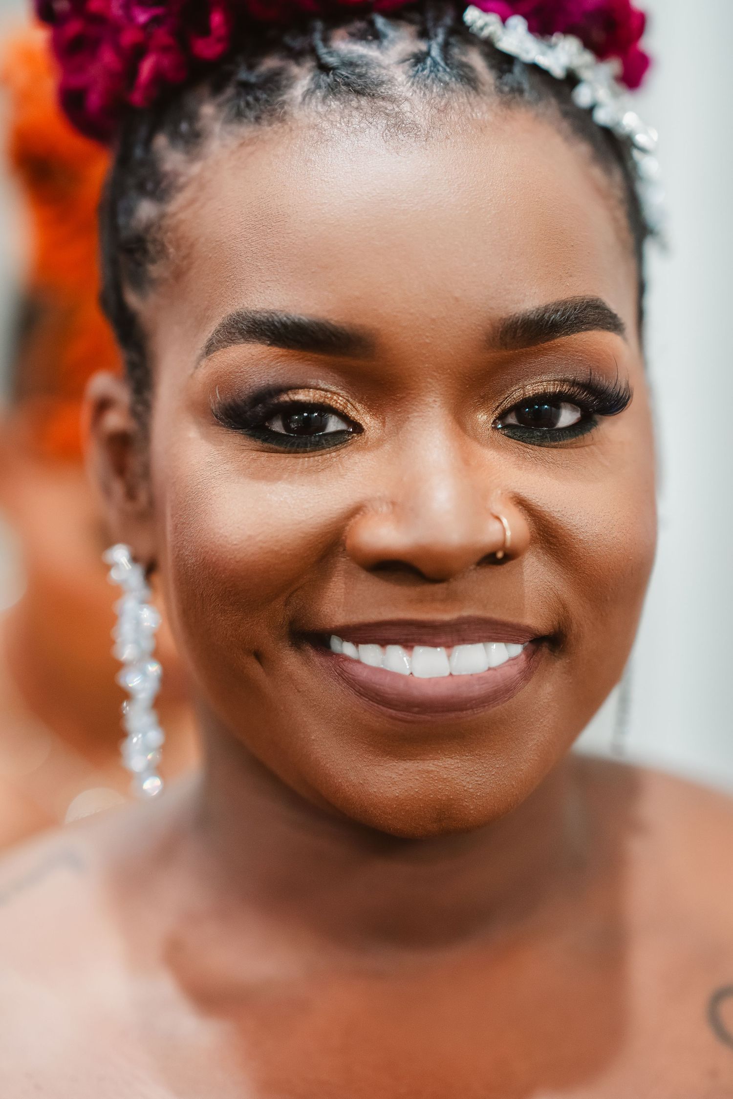 Close up portrait showing a bright smile, elegant bridal makeup, and sparkling earrings against a colorful background.