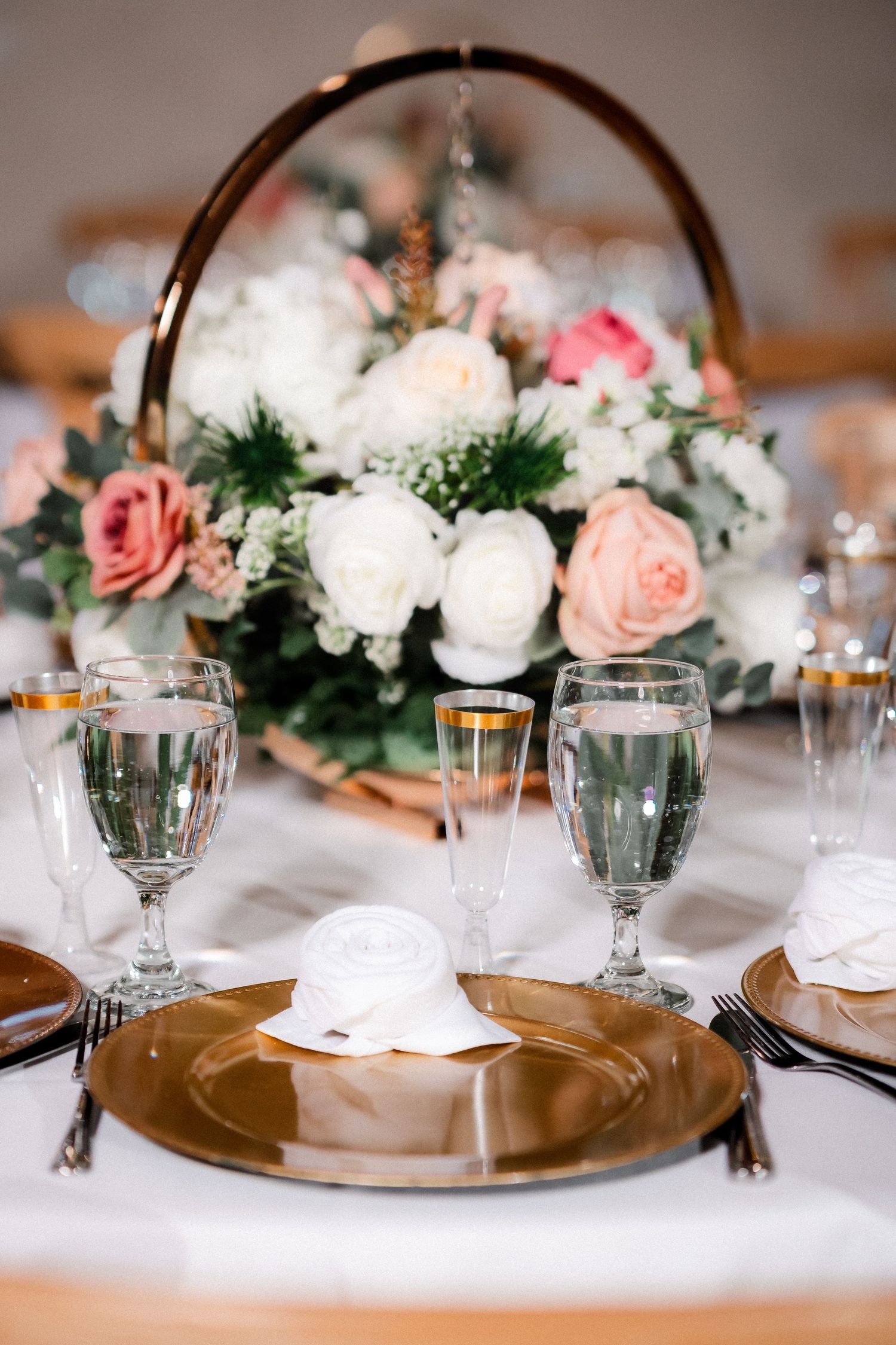Elegant wedding table setting with pink and white floral centerpieces and gold charger plates.
