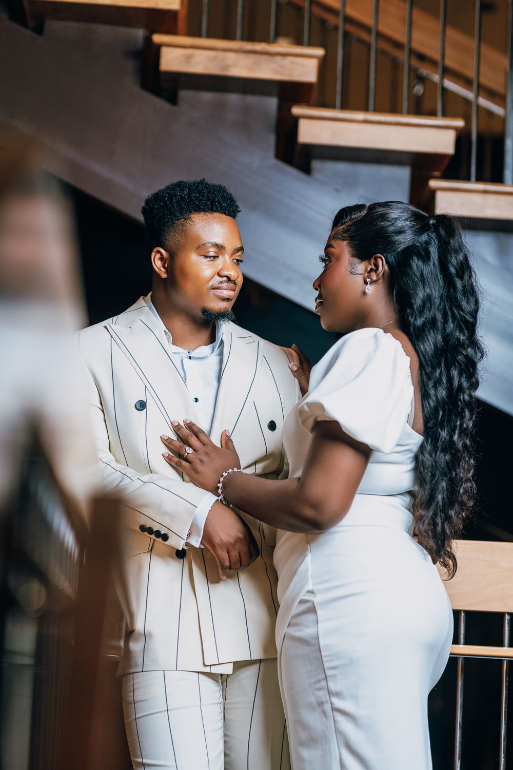Couple wearing coordinated white outfits embrace in an indoor photoshoot.