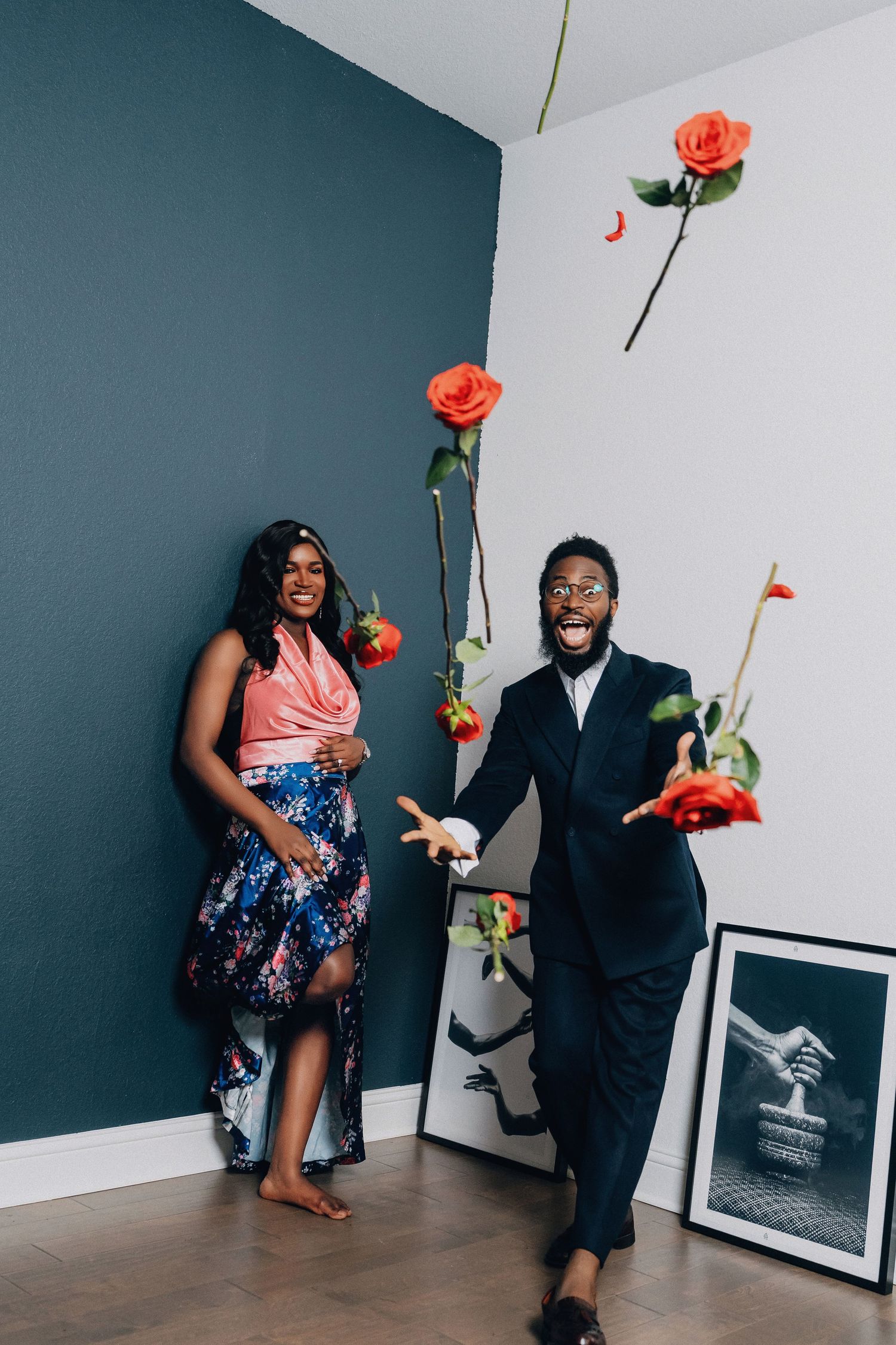 A playful couple dancing with roses against a teal and white wall with framed artwork.