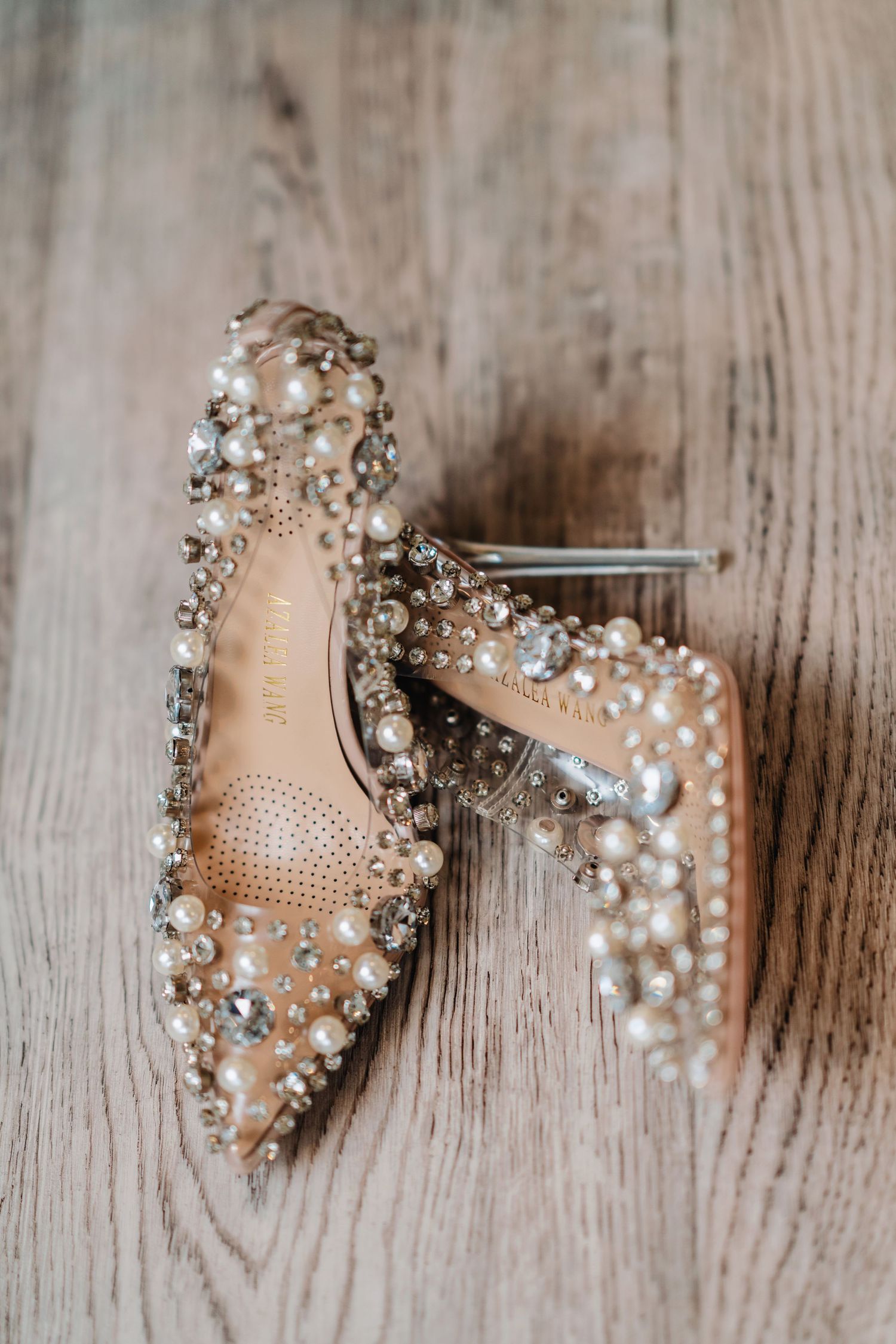 Crystal-embellished nude wedding shoes displayed on wooden surface.