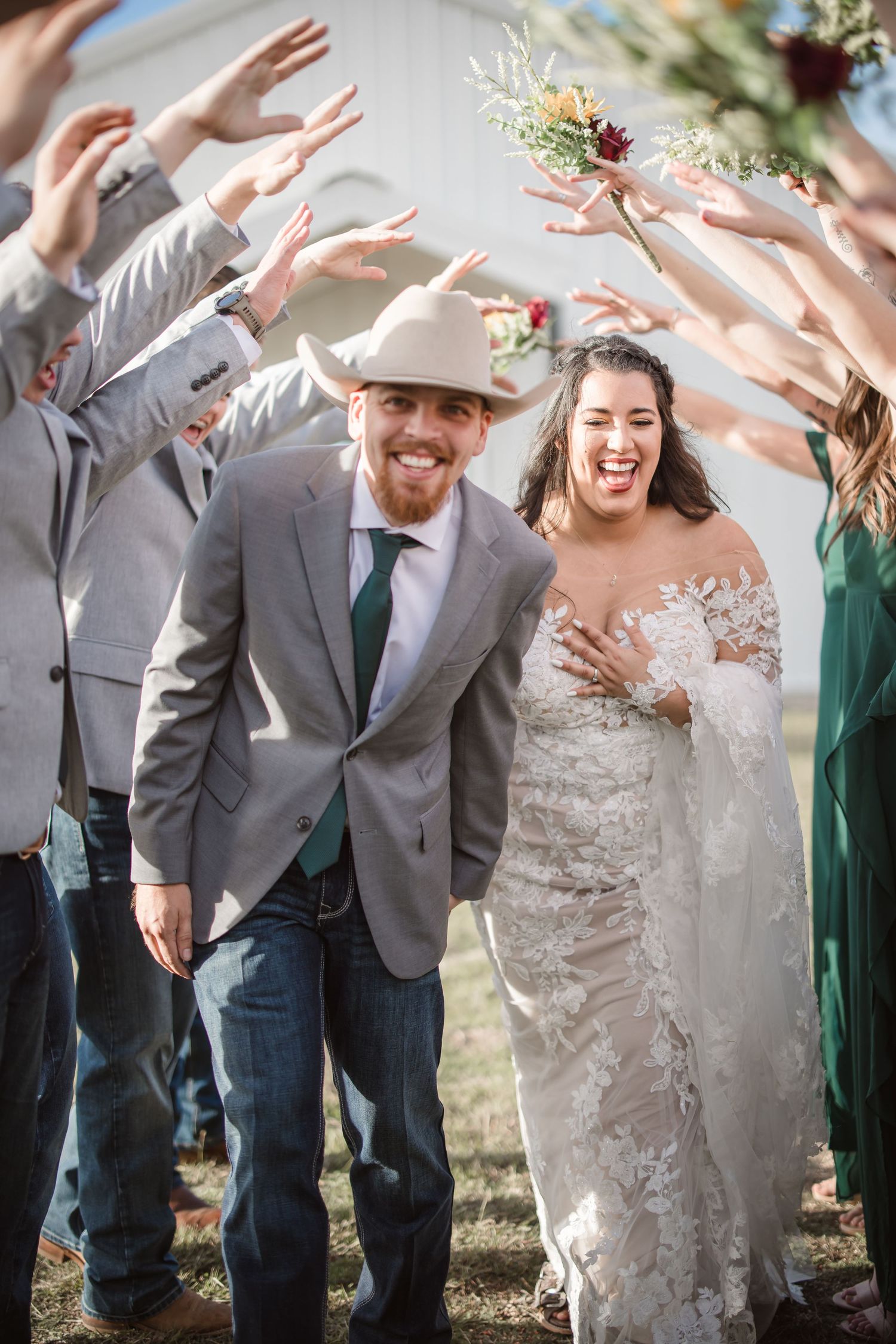 Wedding party celebrates with raised hands in outdoor setting.