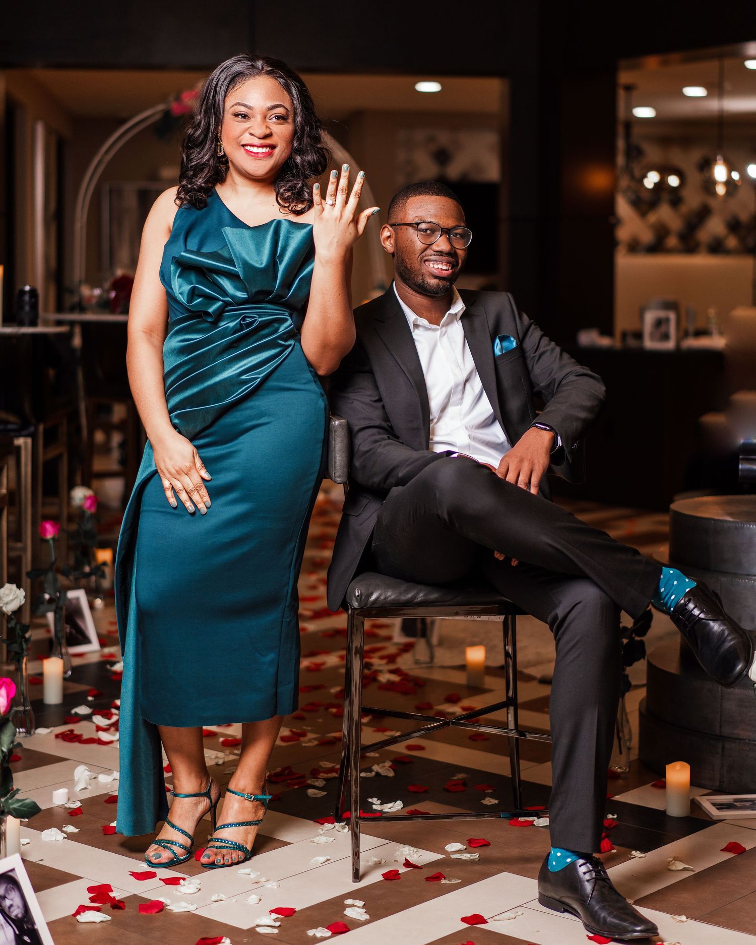 Couple in formal attire poses together during engagement photo session in an elegant indoor setting.