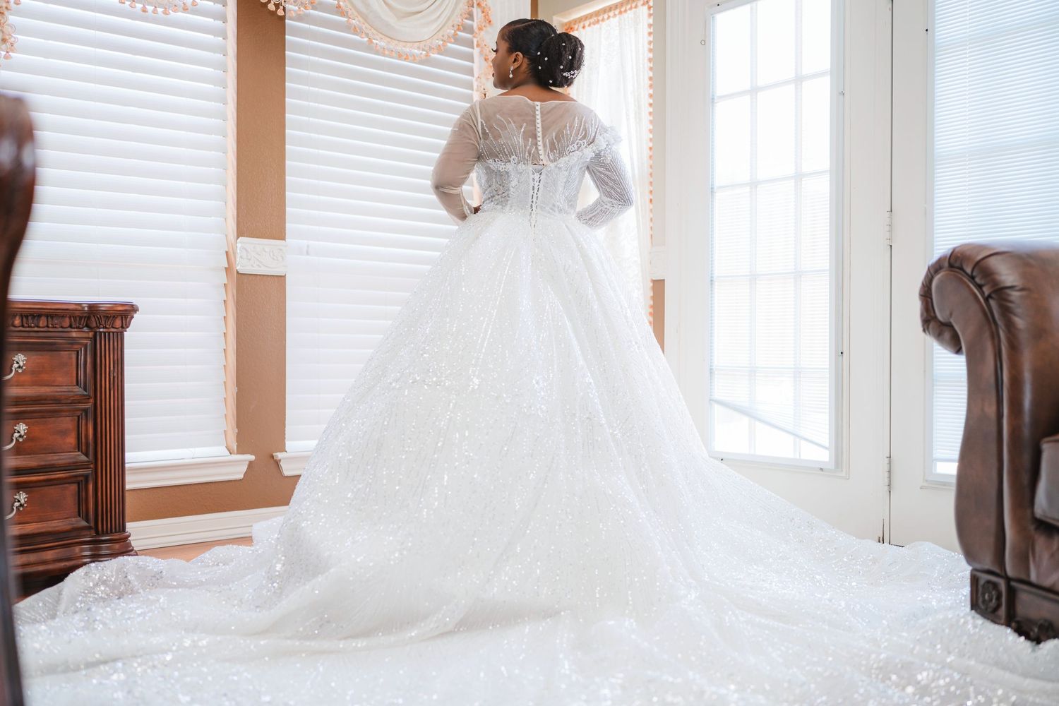 Elegant lace wedding gown with long train photographed from behind in sunlit room.