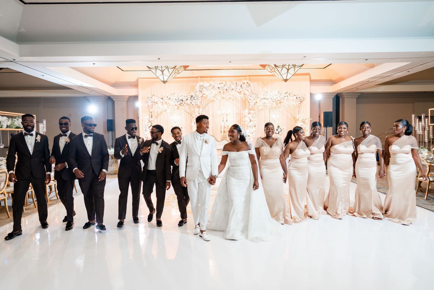 Wedding party members lined up in formal attire at an elegant indoor reception venue.