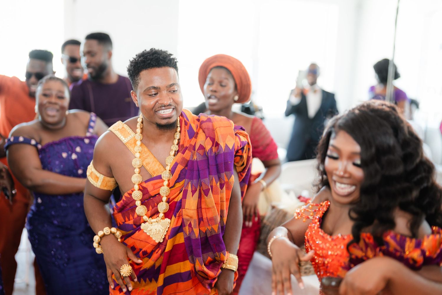 Guests wearing bright orange and purple traditional clothing dance and celebrate together.