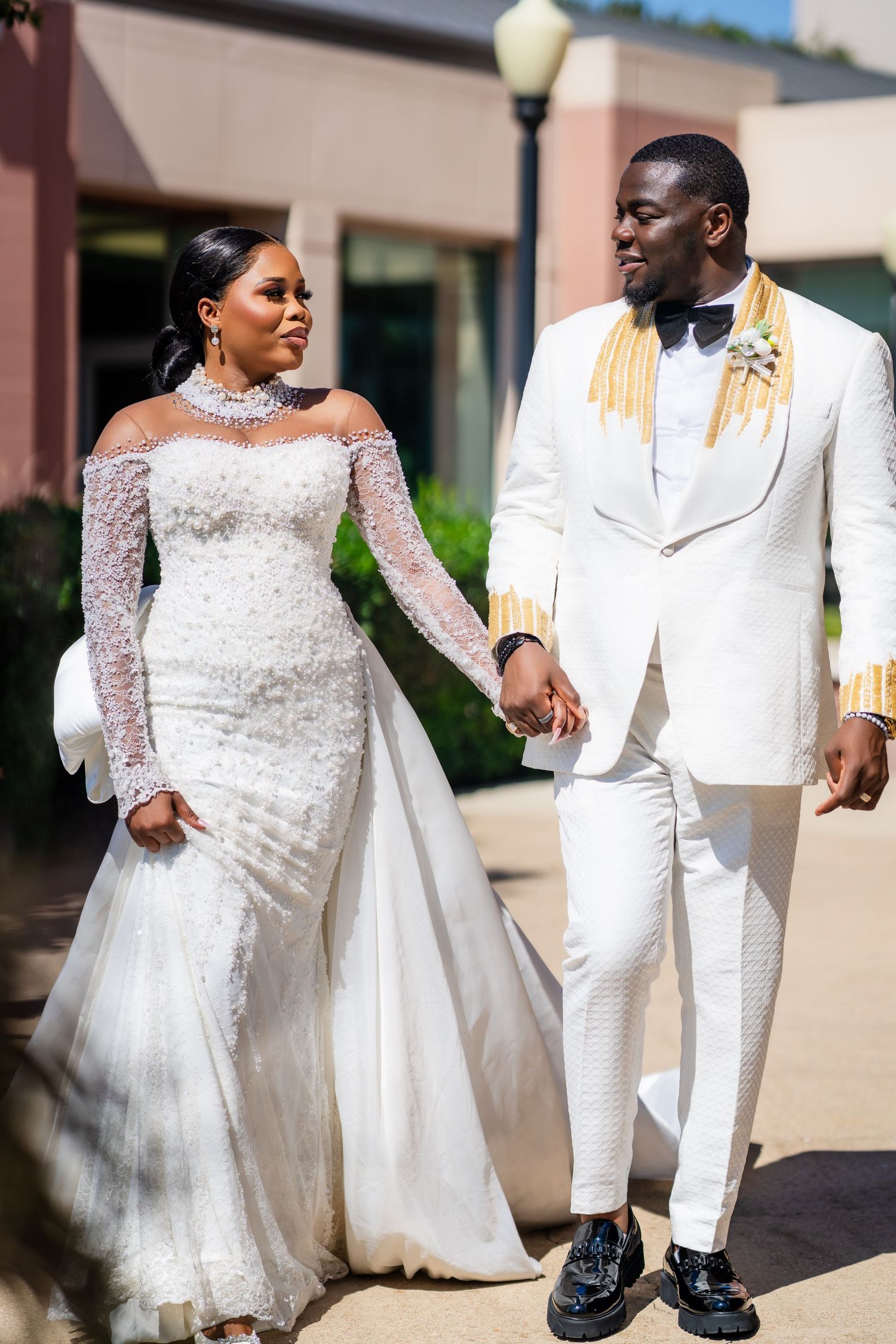 Couple in elegant white wedding attire walking together and sharing joyful moments outdoors.