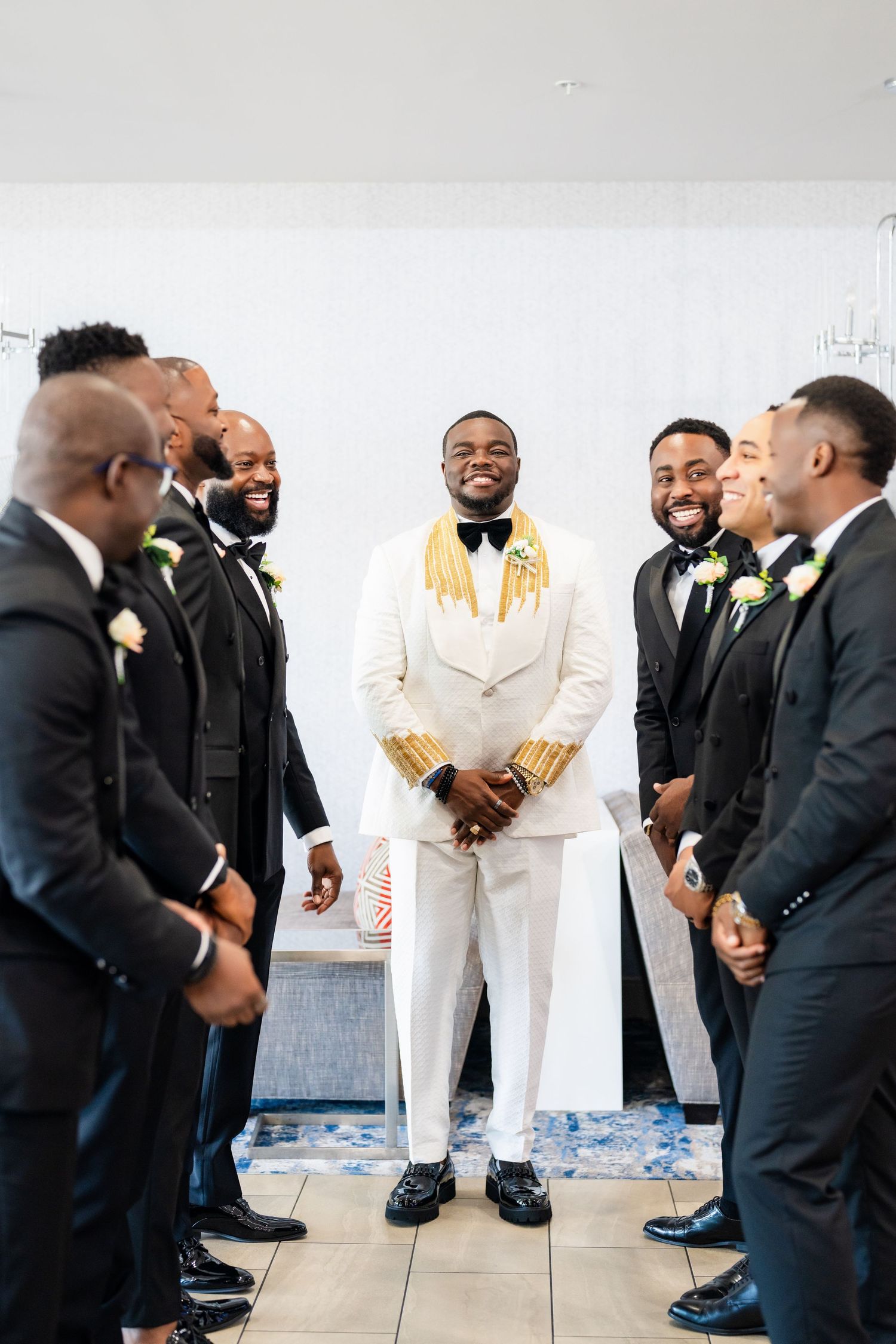 Wedding party gathering with groomsmen in black suits and groom in white tuxedo.