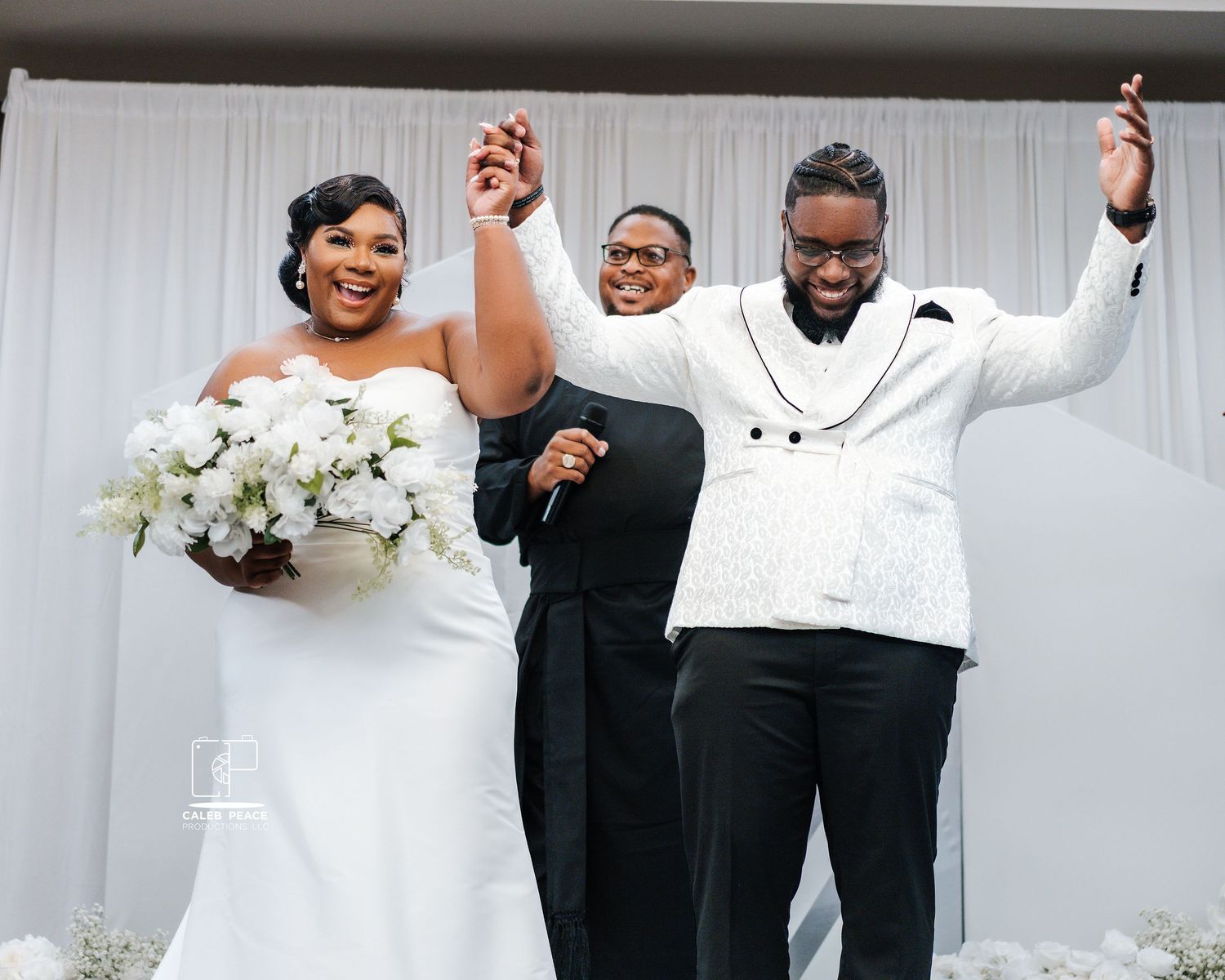 Wedding celebration with guests and wedding party members in formal attire against white backdrop.