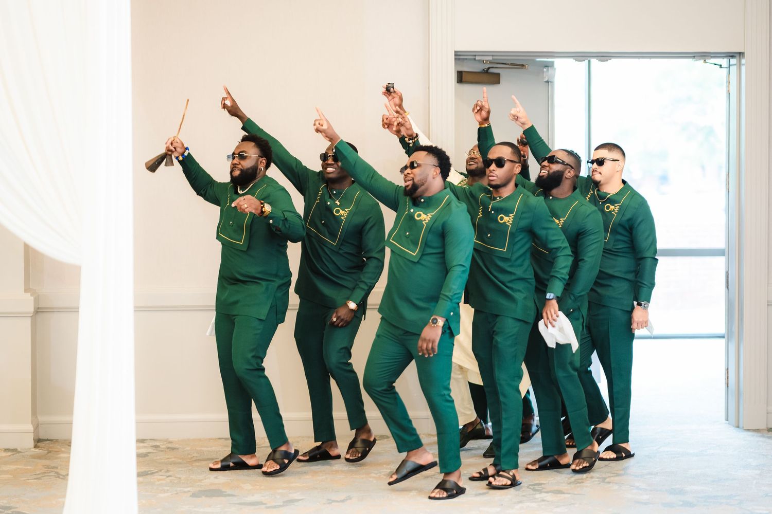 Group wearing matching emerald green outfits performs synchronized dance moves in bright indoor space.
