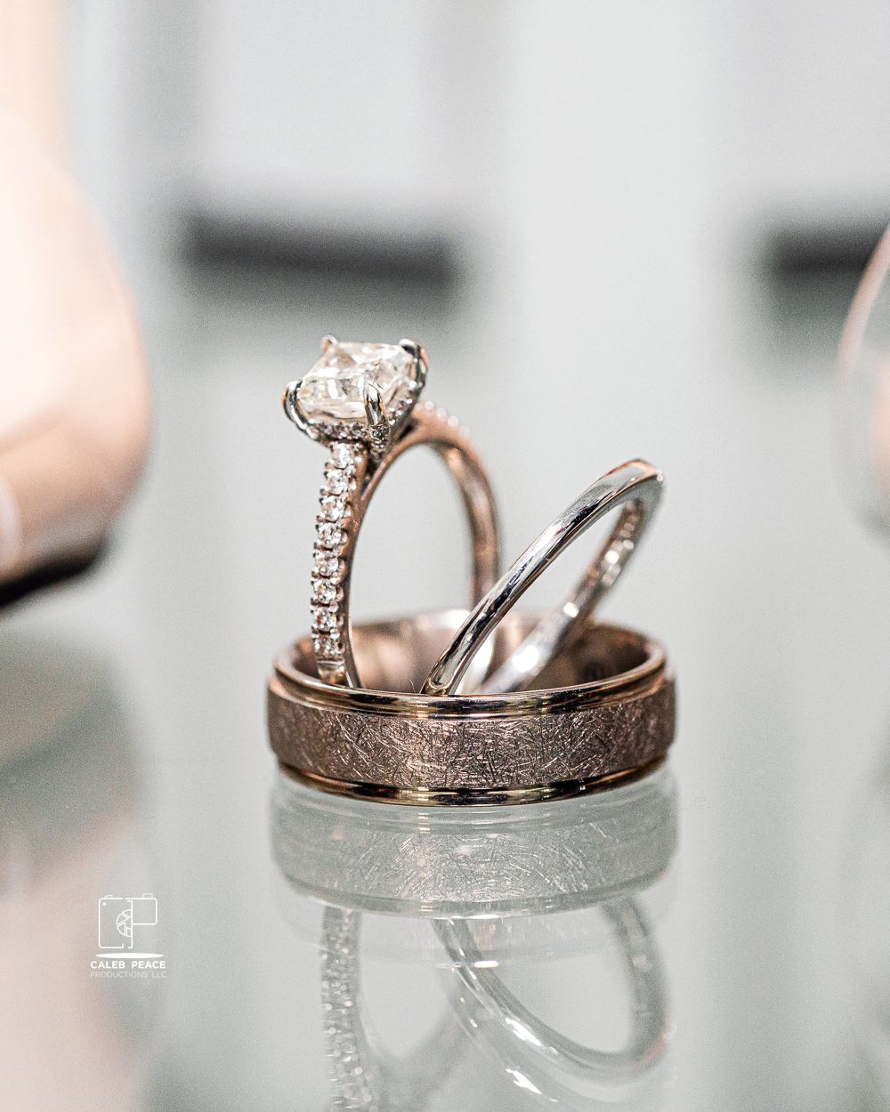 Sparkling diamond engagement ring and wedding bands artistically photographed on reflective surface.