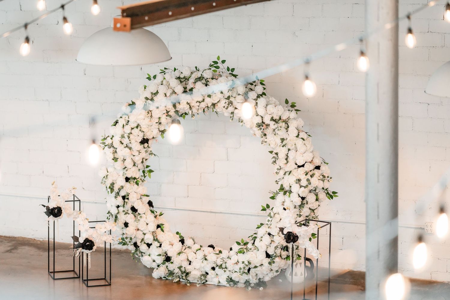 Elegant floral arrangements and string lights decorate a white industrial wedding venue ceiling.