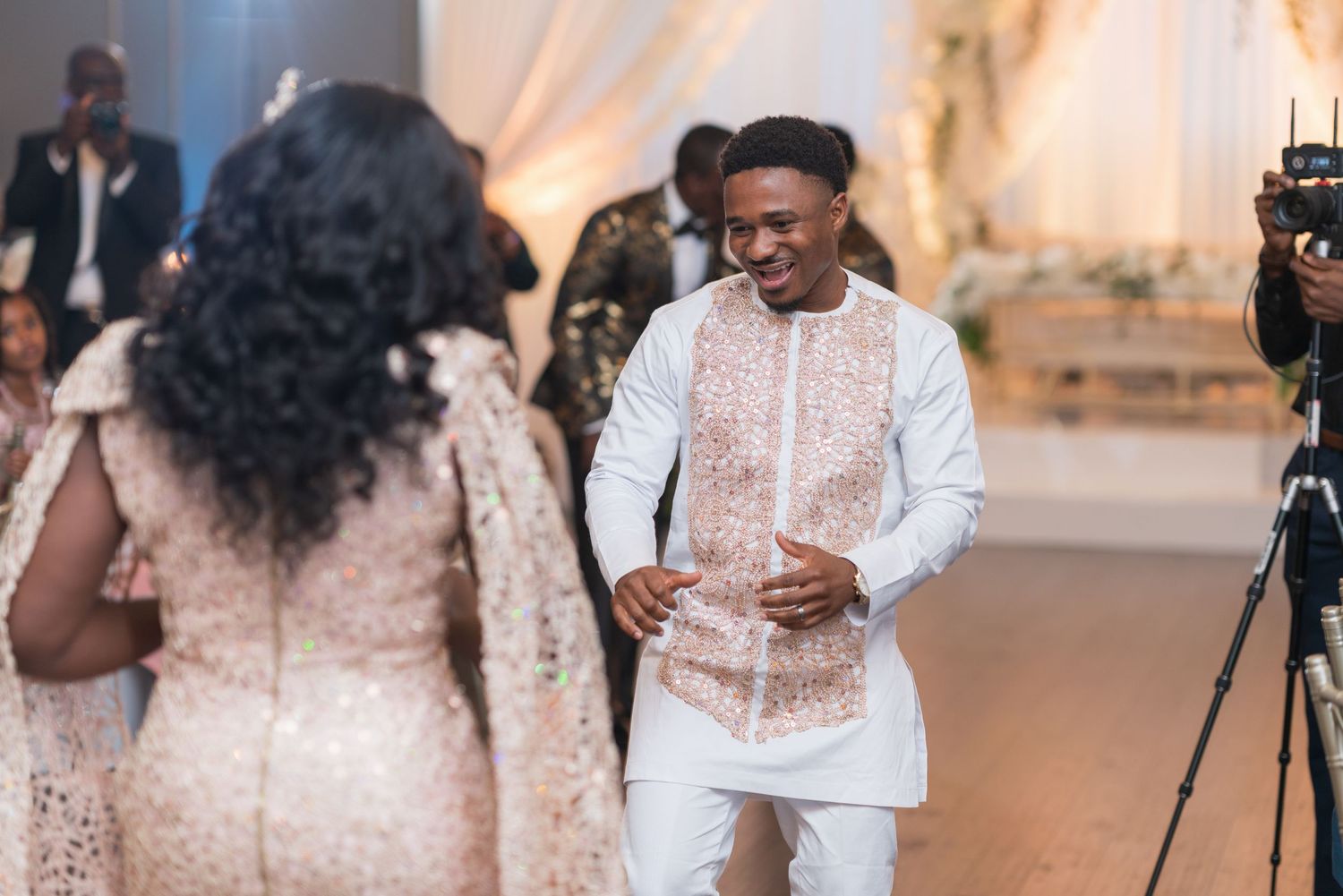 Wedding reception scene with elegant white and gold decor and dancing guests.