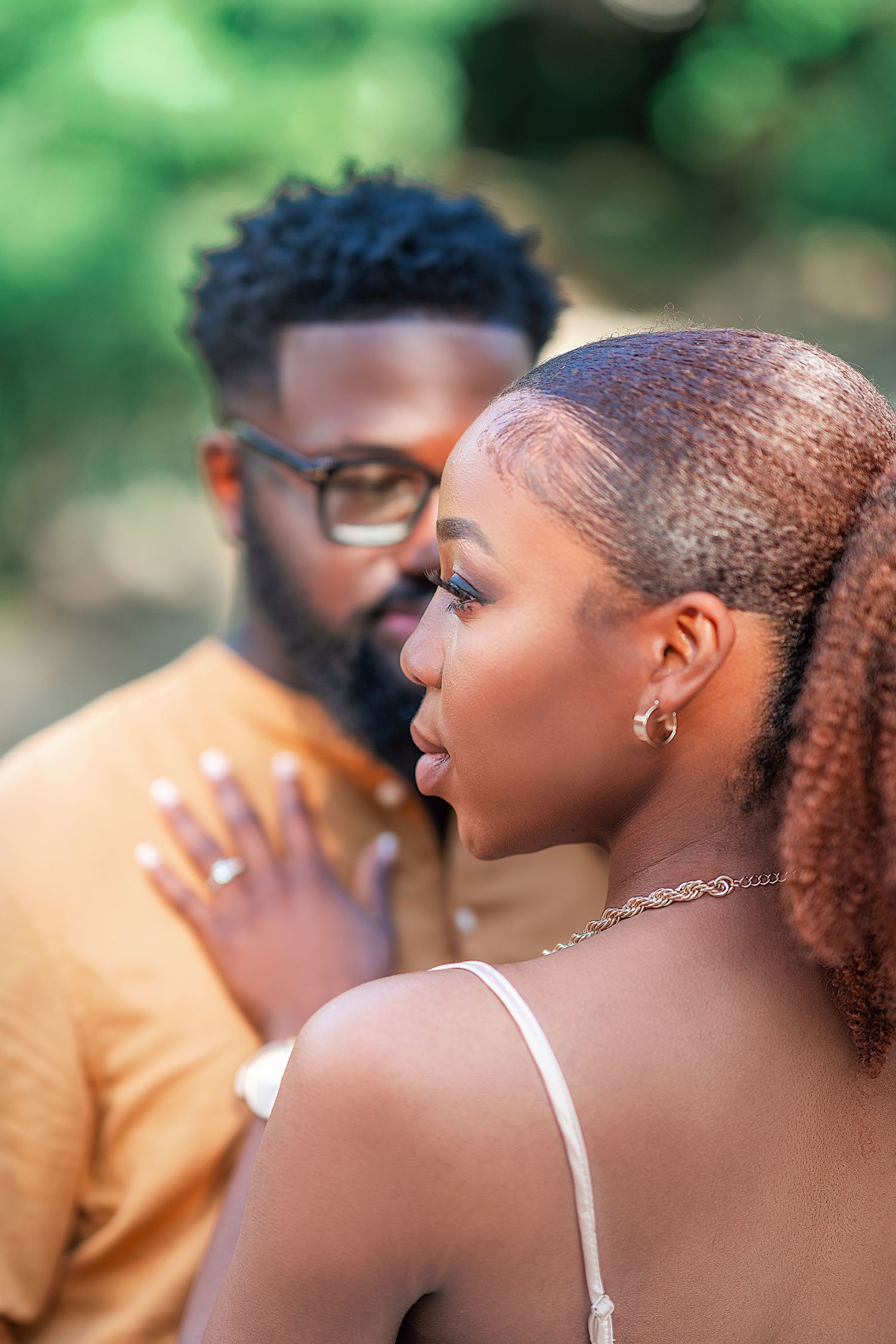 A romantic couple poses outdoors in a garden setting with soft bokeh background.