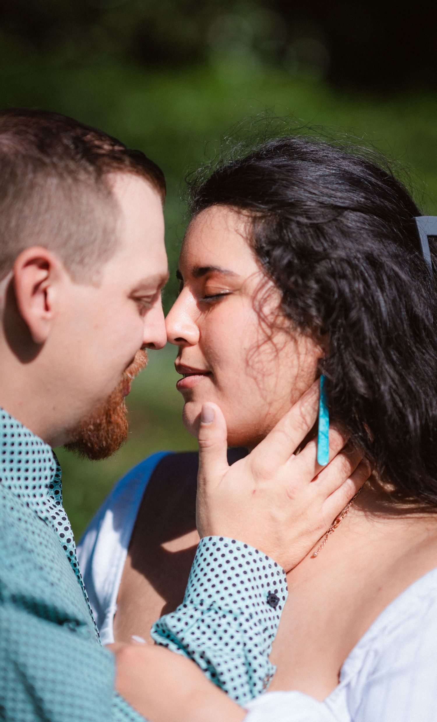 An intimate moment captured in a garden as a couple shares a tender embrace against a blurred green background.