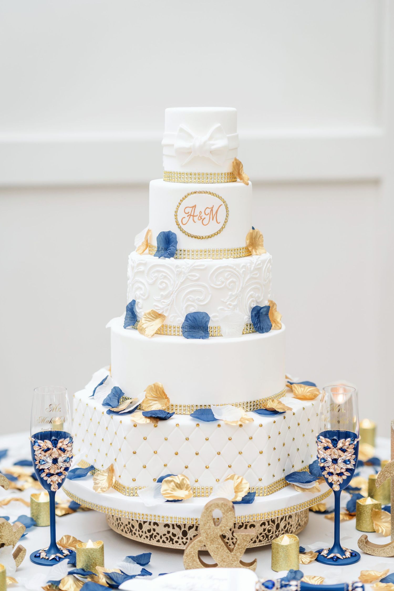 Elegant tiered wedding cake with white, blue and gold details displayed on decorative stands.