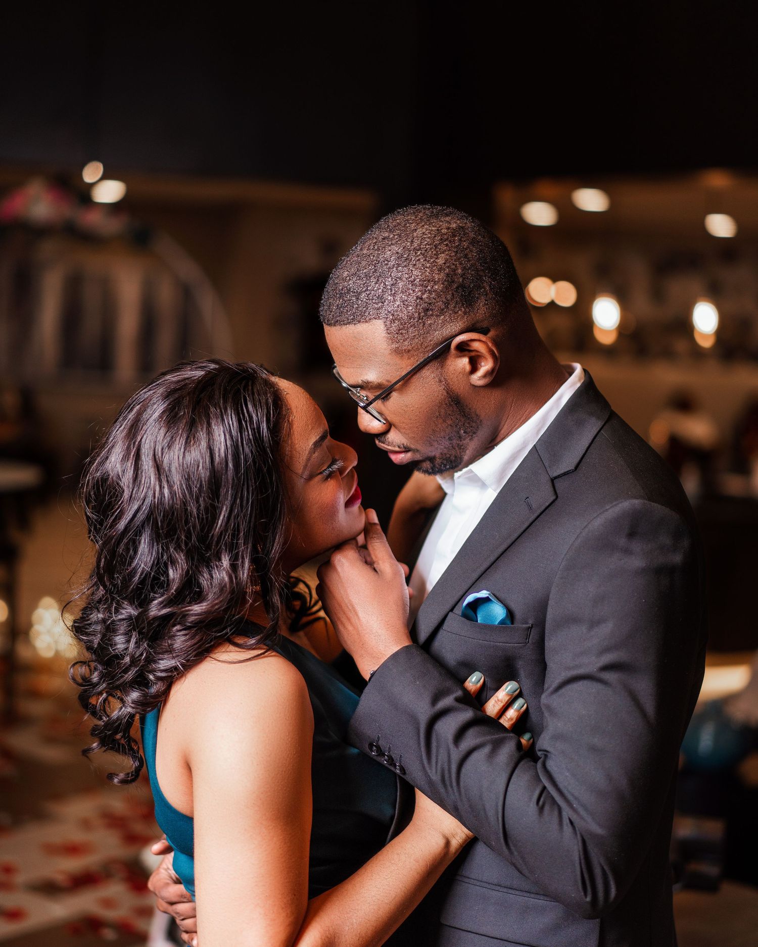 Romantic couple shares intimate moments in formal attire during an evening celebration with soft lighting.
