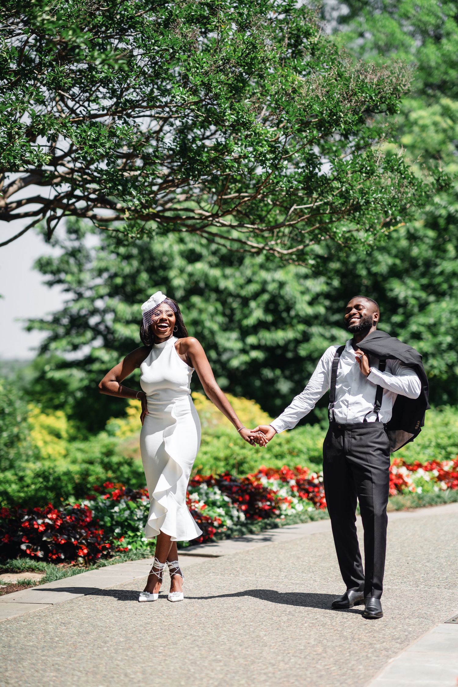 A couple dances playfully in a garden with red flowers and lush greenery in the background.