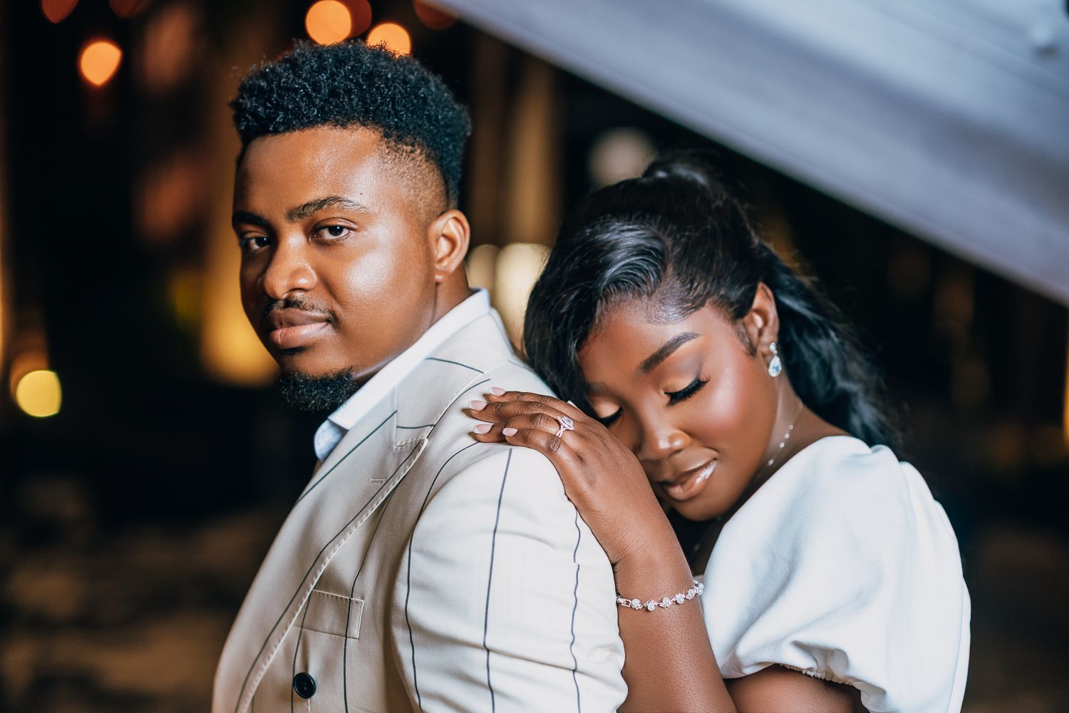 Couple shares joyful laughter during romantic indoor photo session with warm lighting.