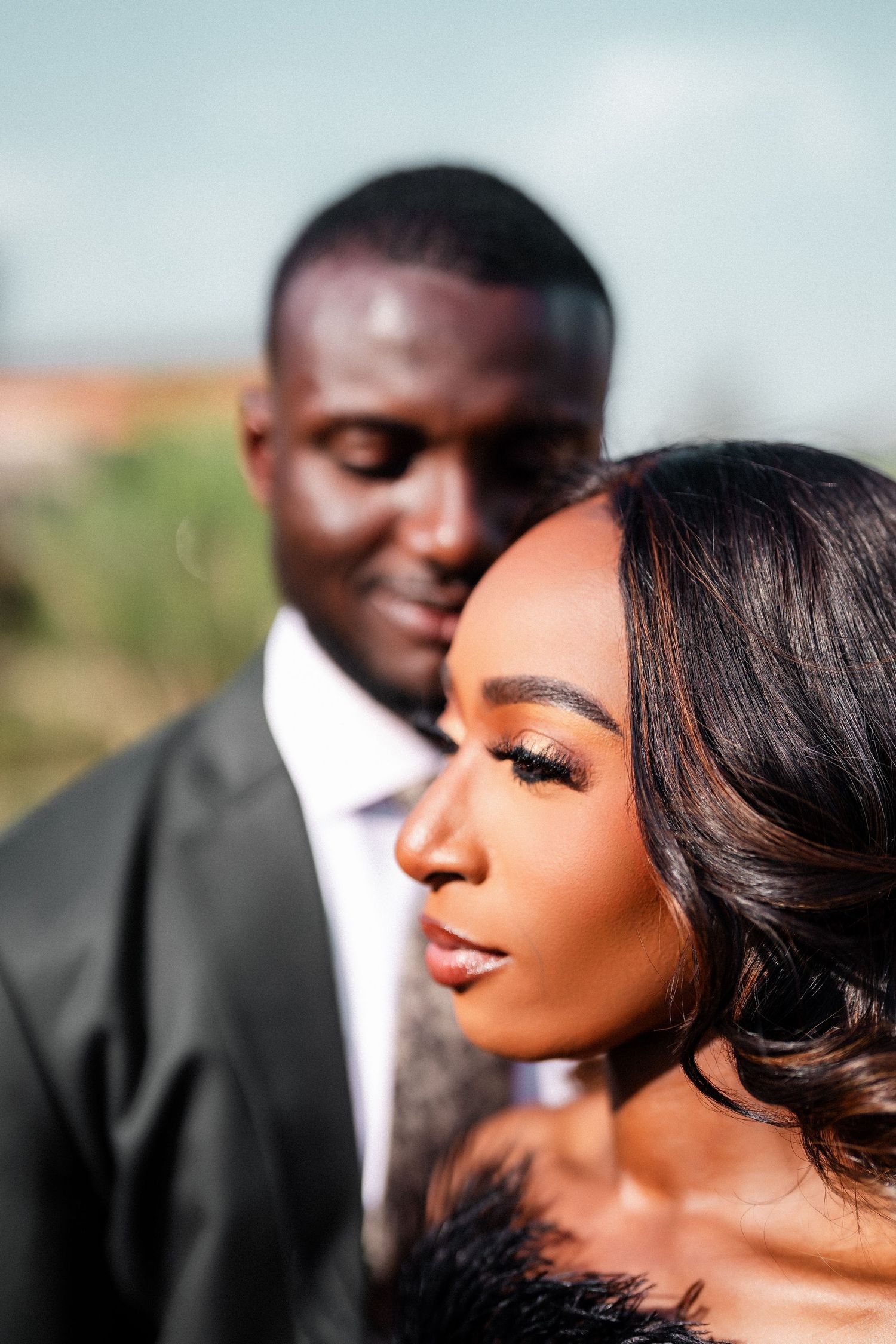 Romantic close-up portrait of couple in formal wear against blurred outdoor background.